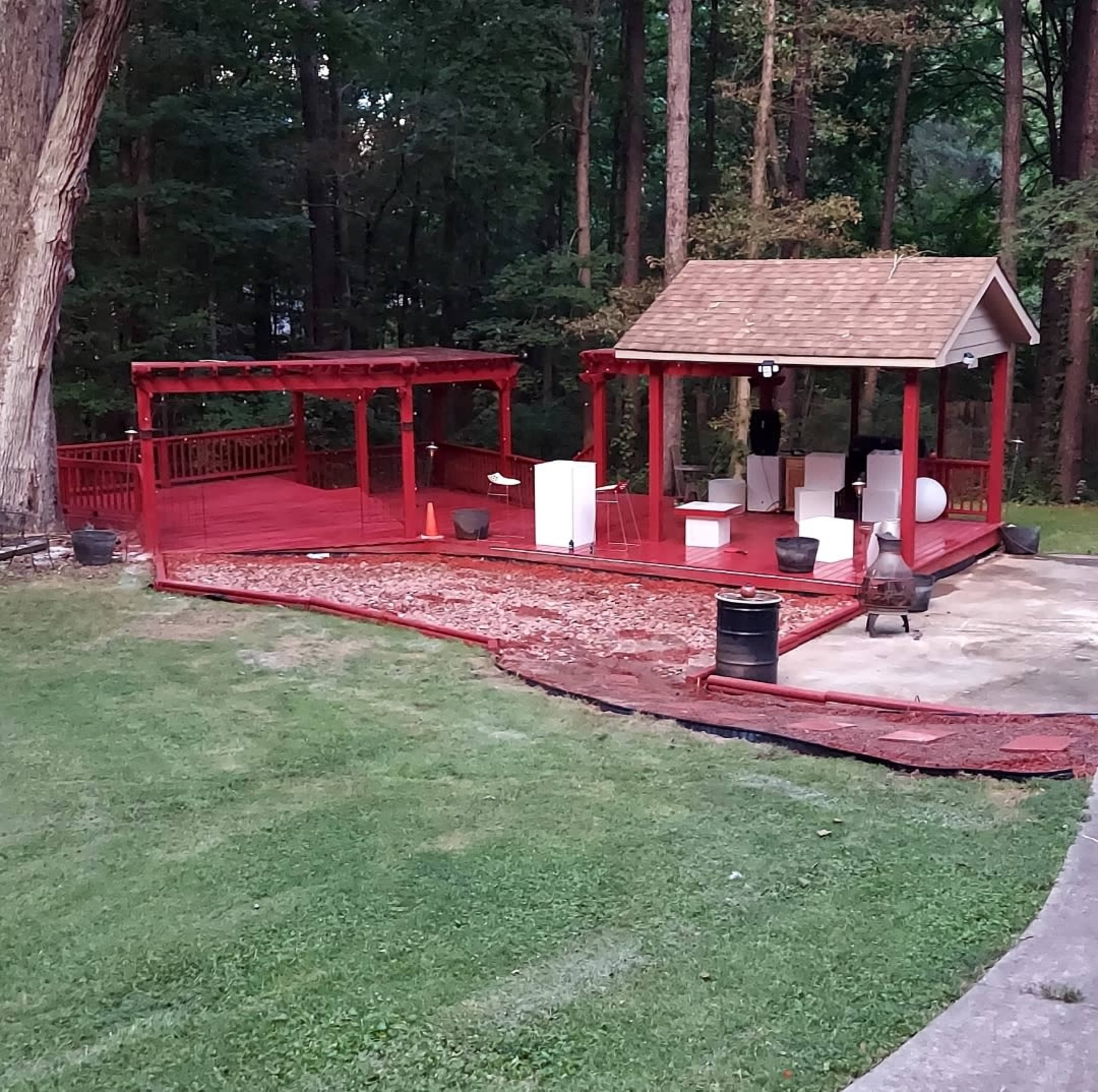 A red wooden deck with a gazebo and various outdoor furniture set in a wooded area.