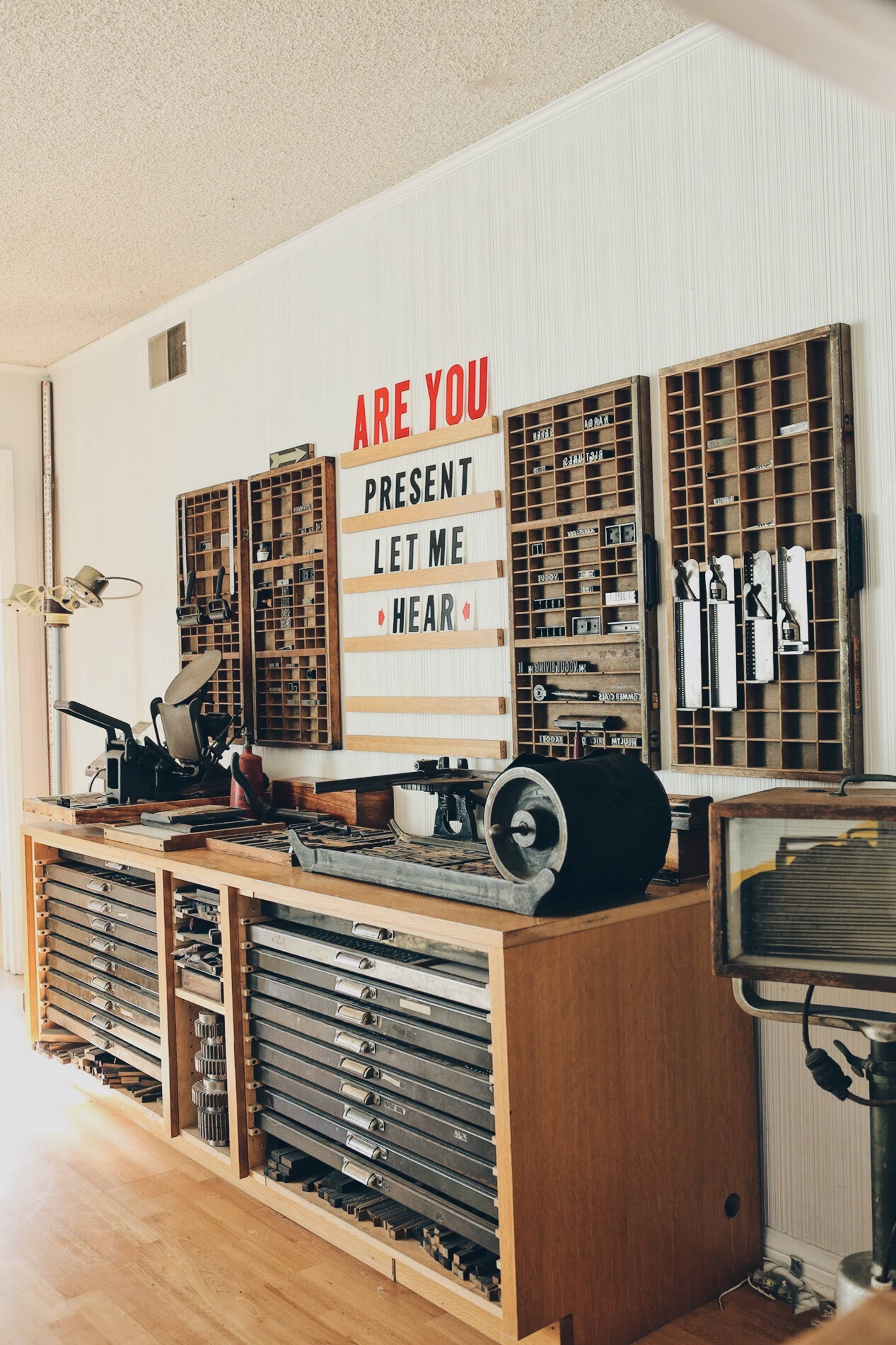 A wooden workbench is lined with various tools and an organized display of letters, conveying the message "ARE YOU PRESENT LET ME HEAR."