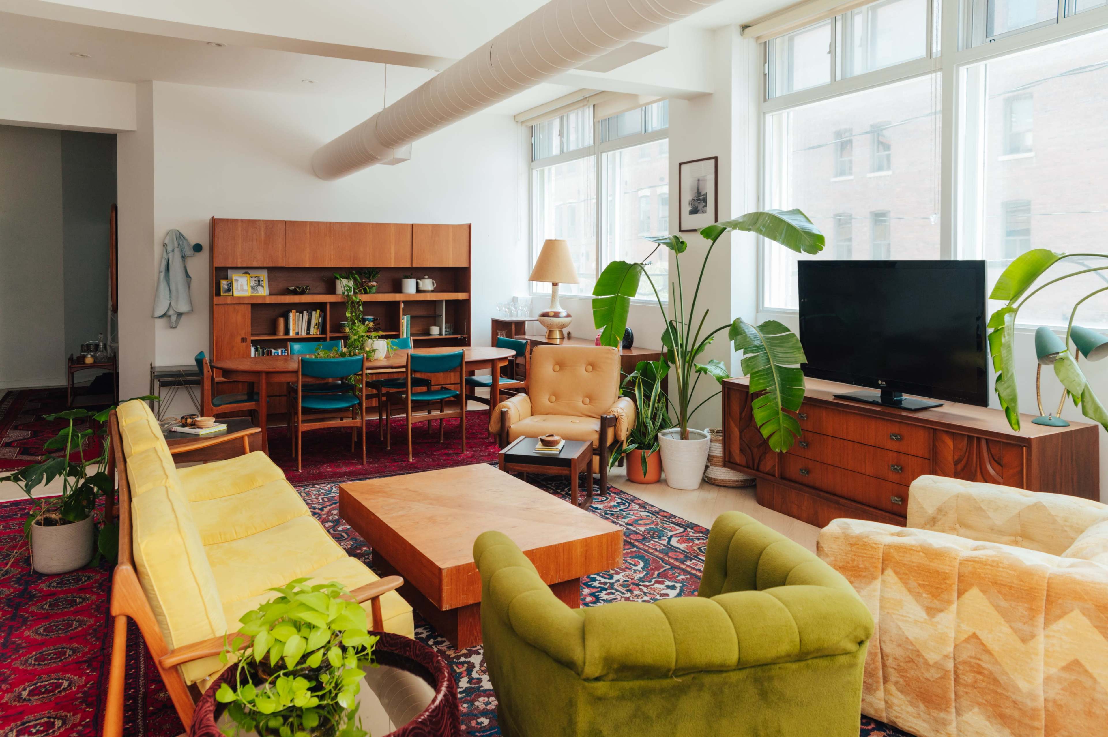 A spacious living room features a mix of colorful seating, a wooden coffee table, and large windows that allow natural light to fill the space.