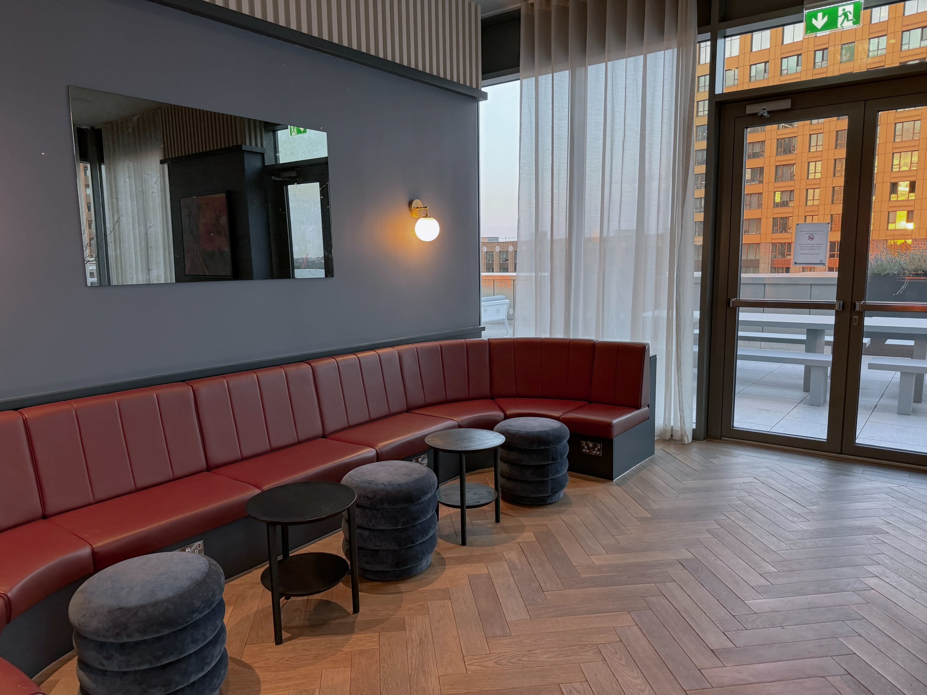 A modern lounge area with a curved red bench, small round tables, and large windows providing natural light.