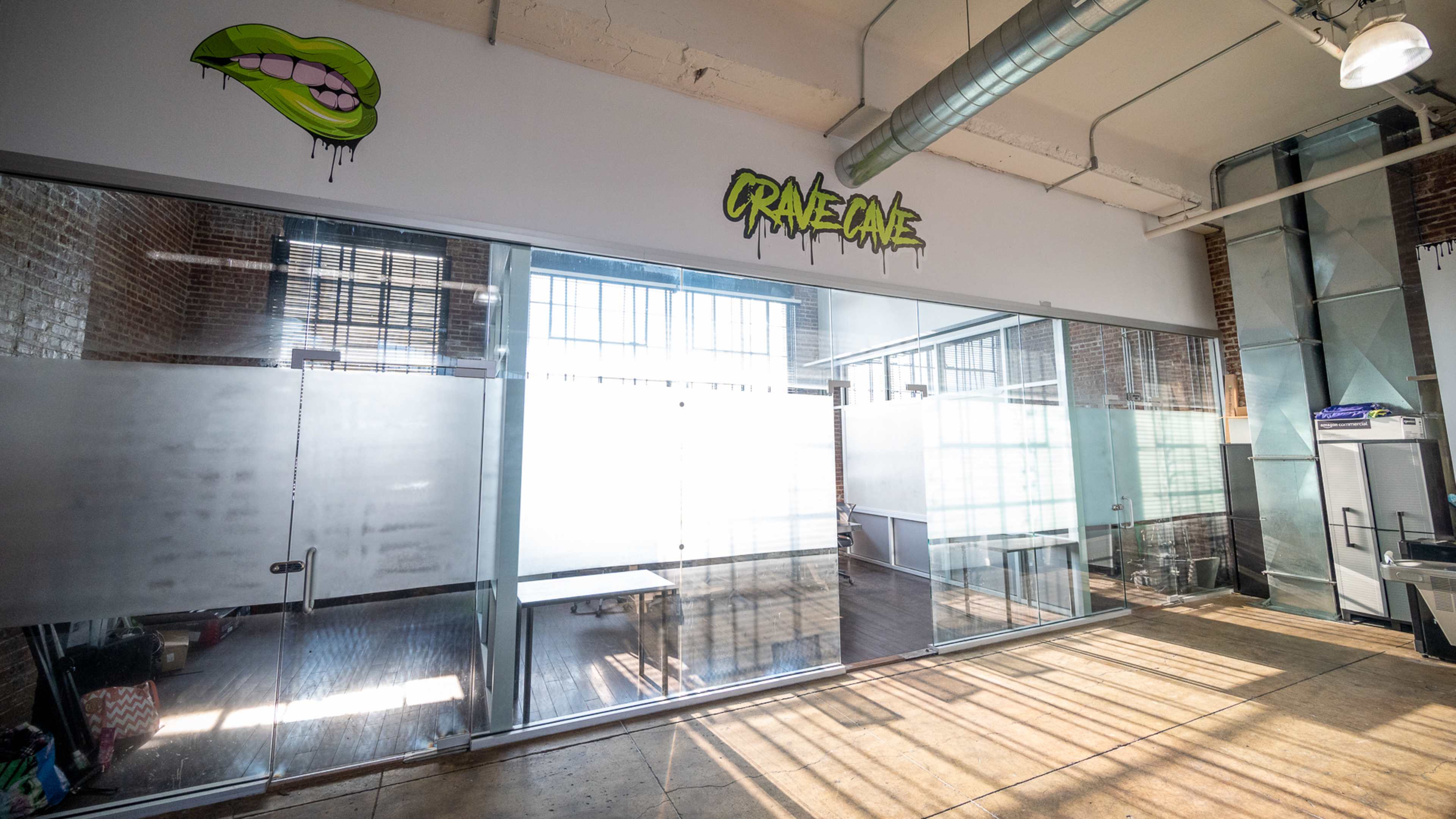 A modern office space with large glass walls, featuring a graffiti-style logo on the wall and natural light streaming in through the windows.