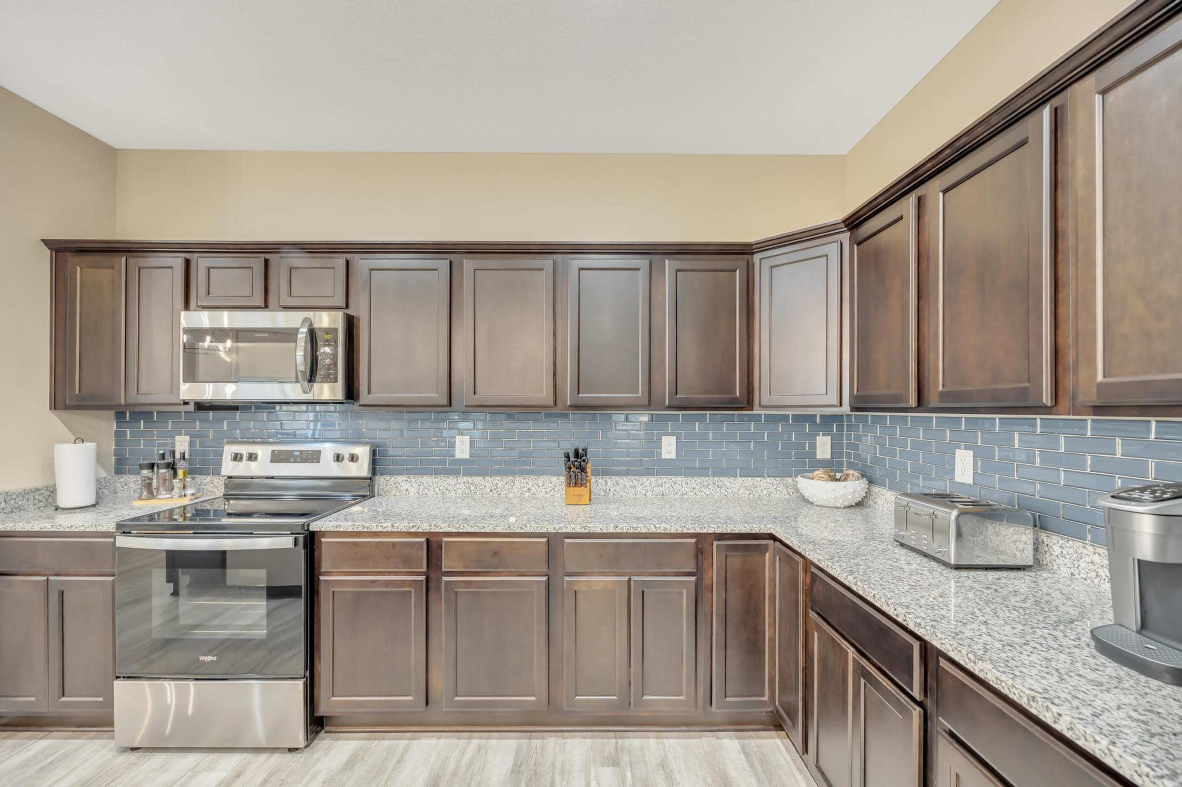 The image shows a modern kitchen with dark wood cabinetry, granite countertops, and stainless steel appliances, featuring a blue tile backsplash.