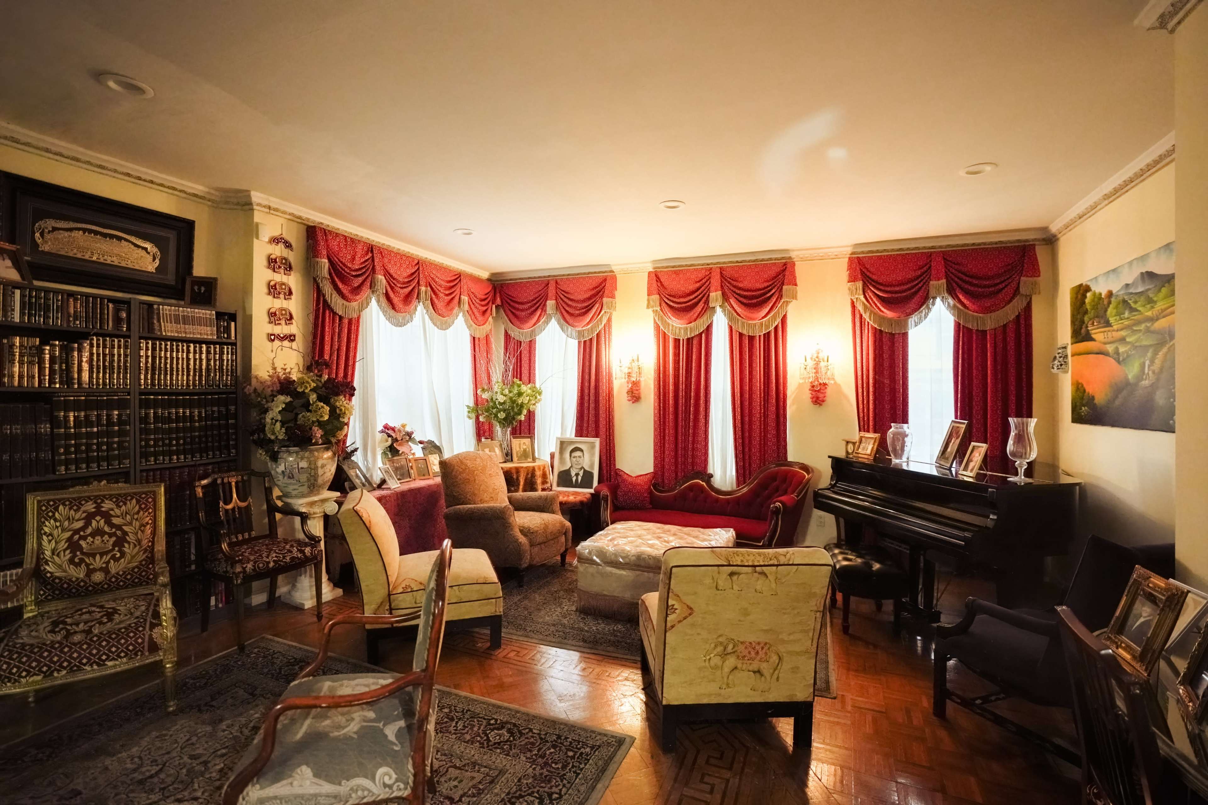 The image depicts an elegantly furnished living room with ornate drapes, a piano, and various framed photographs and artworks on display.