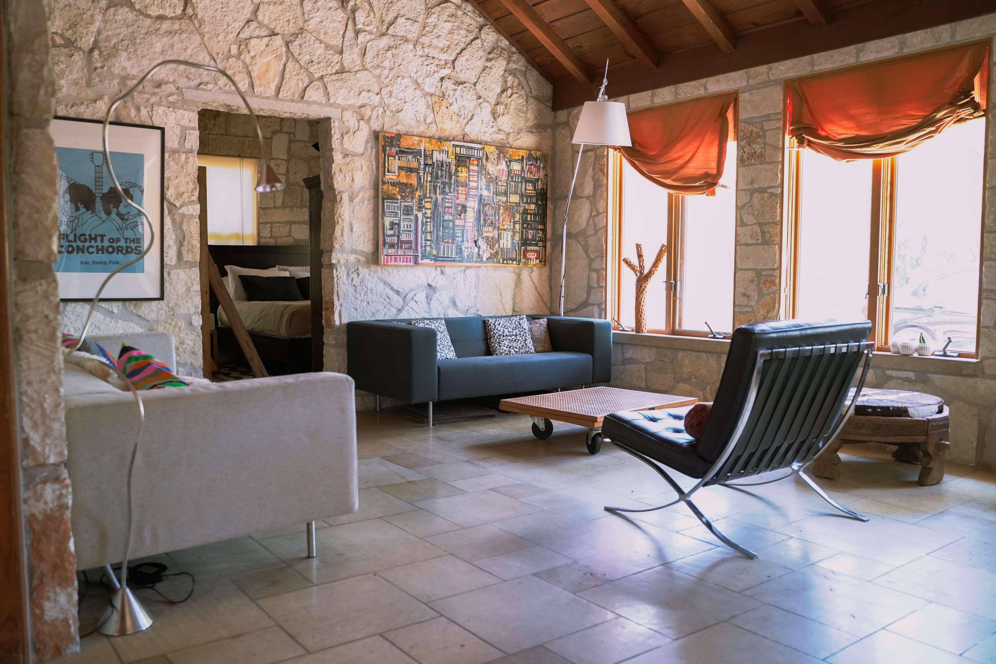 A living room with stone walls, wooden beams, and a mix of modern furniture, including a gray sofa and a black lounge chair.