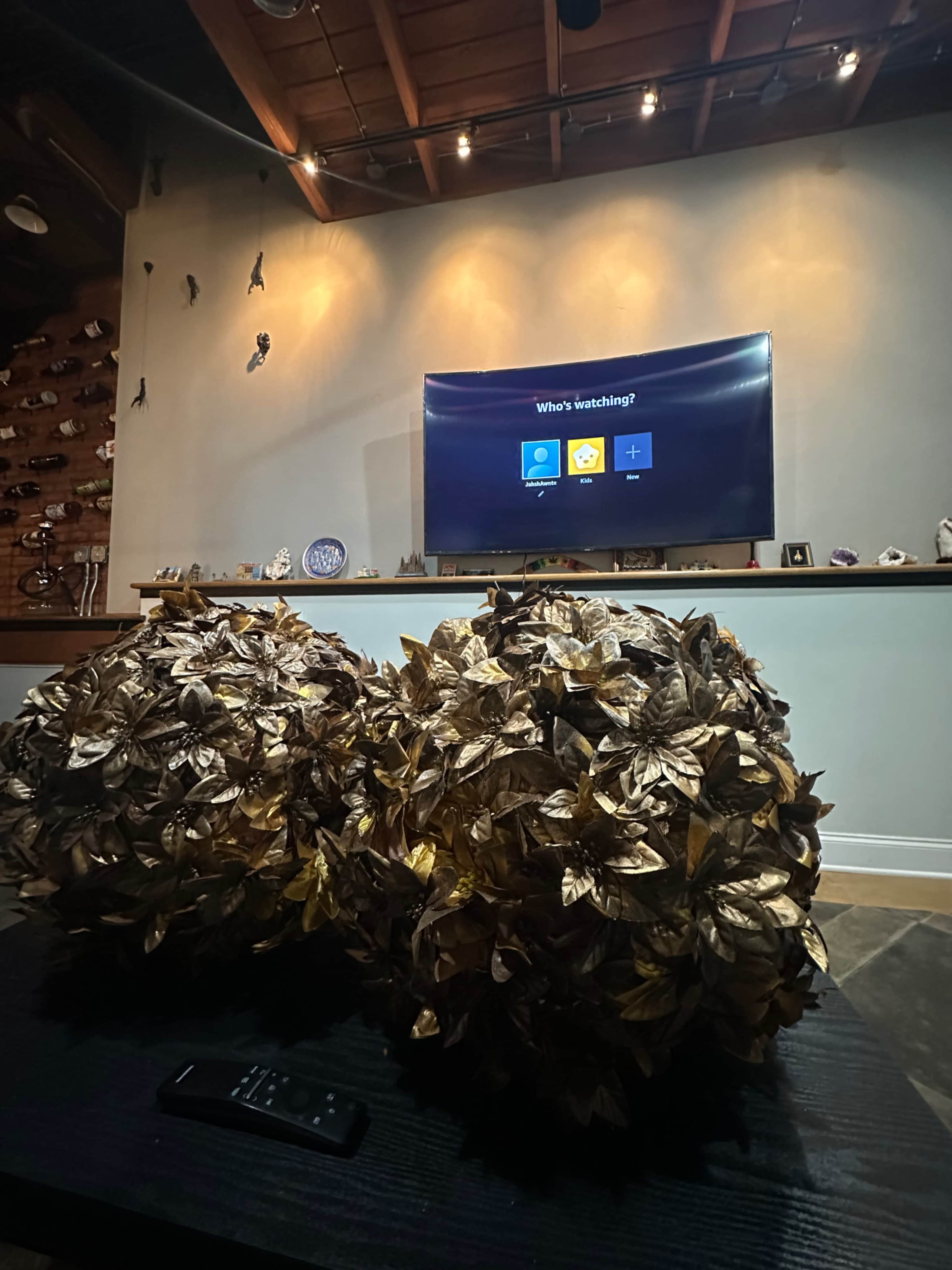 A cozy living room features a dark coffee table with two decorative floral arrangements in front of a television displaying a streaming service menu on the wall.