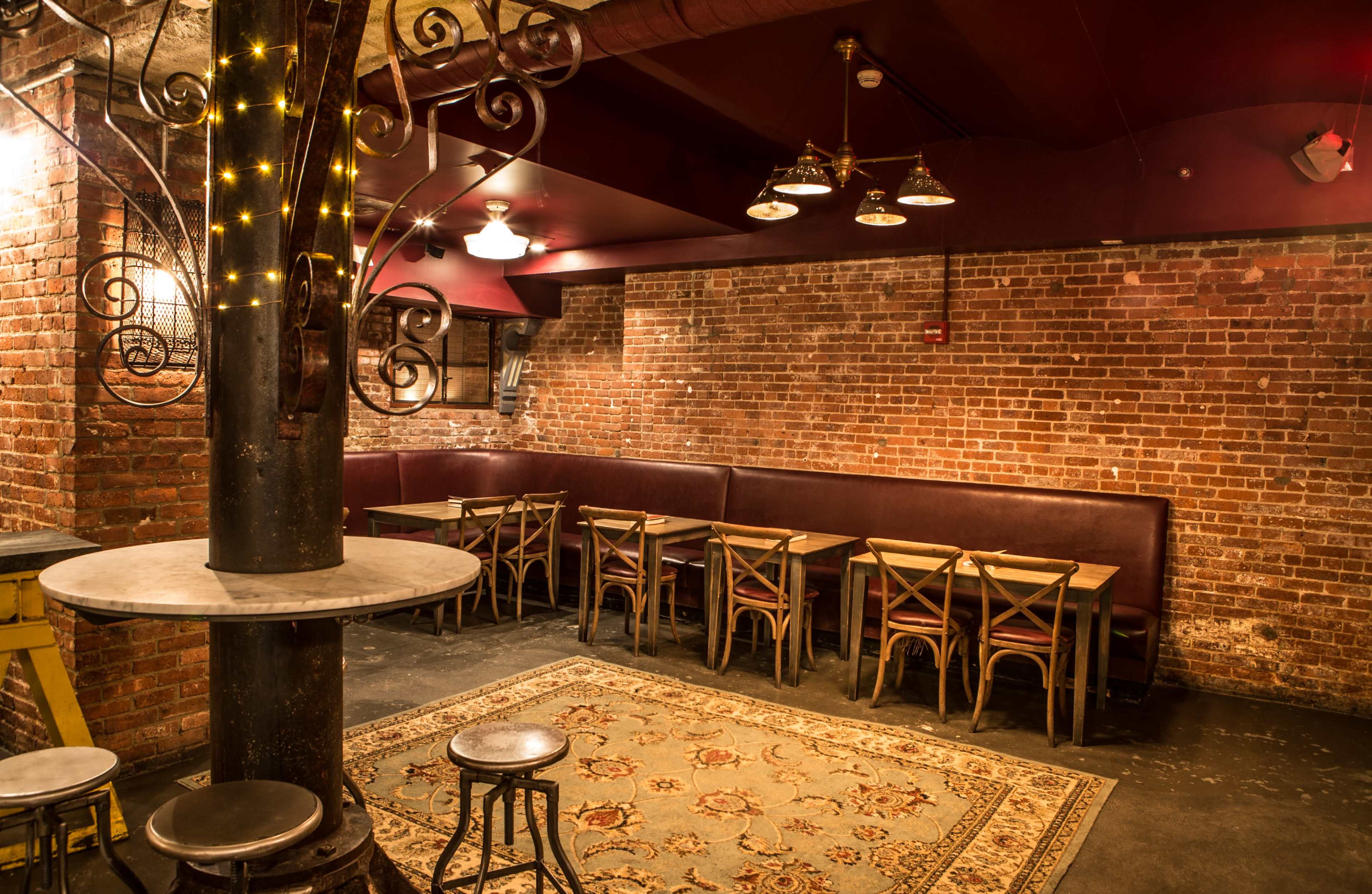 The image shows a rustic restaurant interior with exposed brick walls, wooden tables and chairs, and a patterned rug on a dark floor.