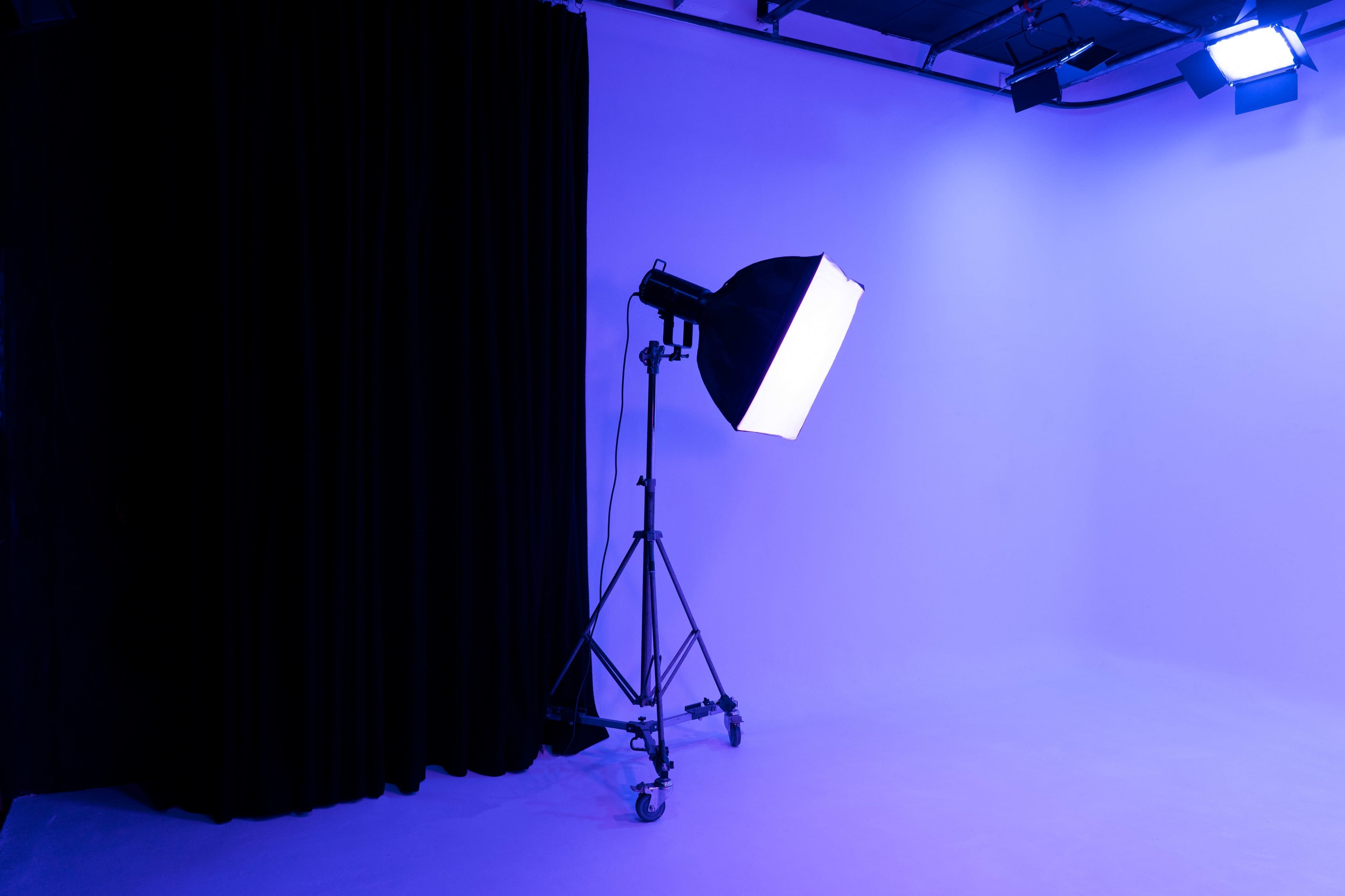 The image shows a photography studio with purple walls, a large softbox on a stand, and a black curtain in the background.