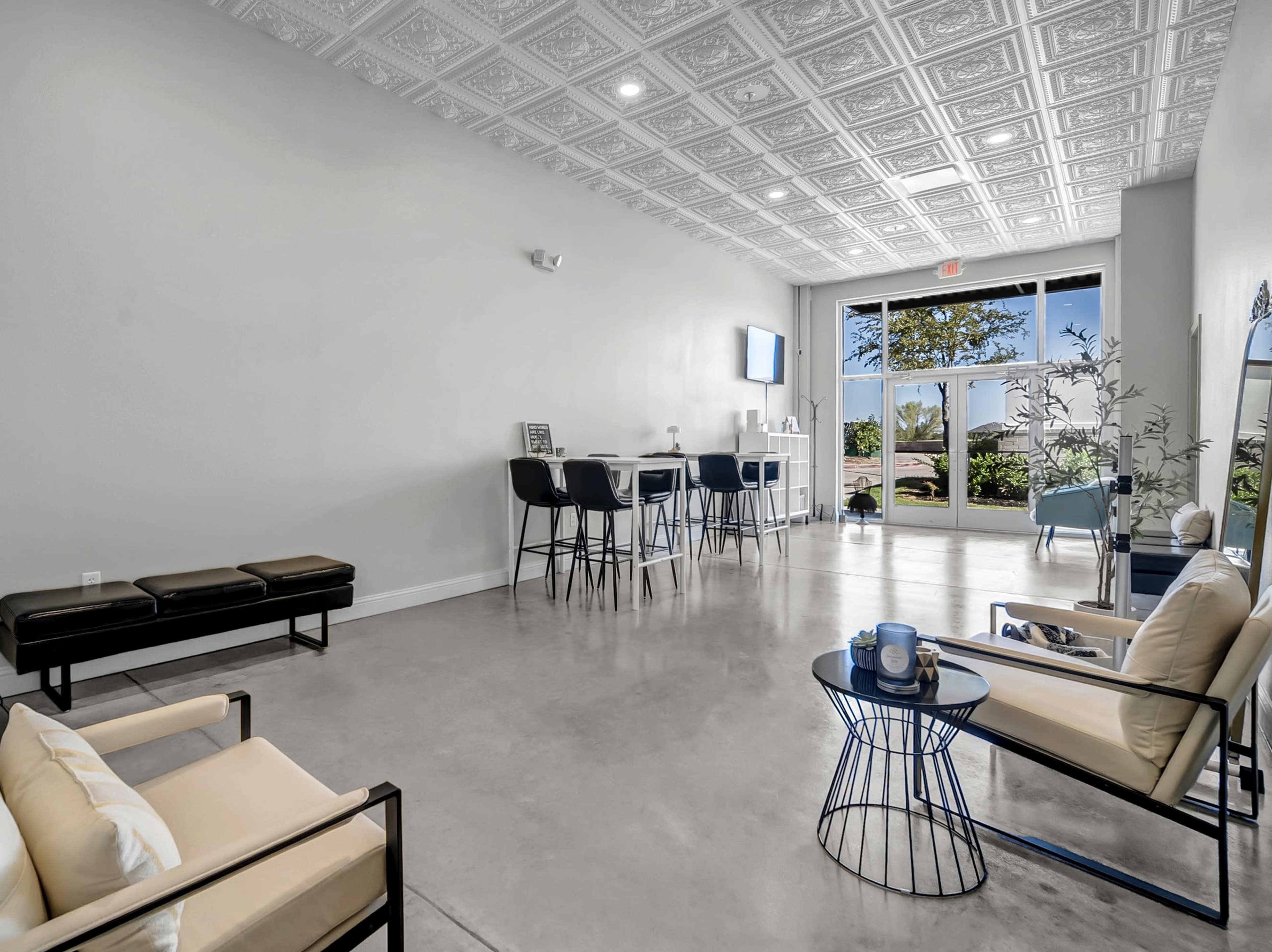 The image shows a modern, minimalist reception area featuring chairs, a small table, and a large window with outdoor views.