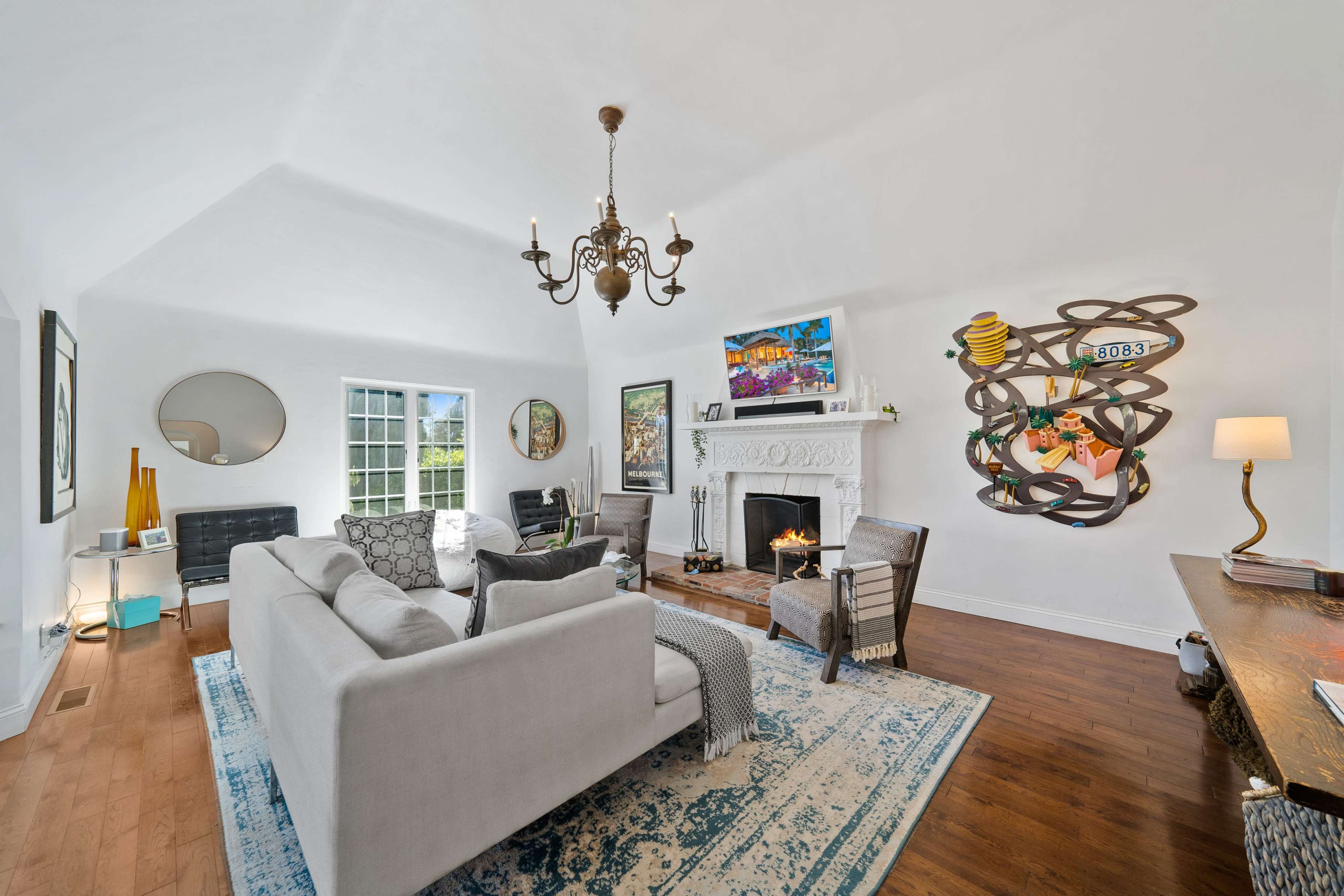 The bright living room features a stylish sofa, a fireplace with decorative art pieces, and a mix of modern and traditional furnishings.