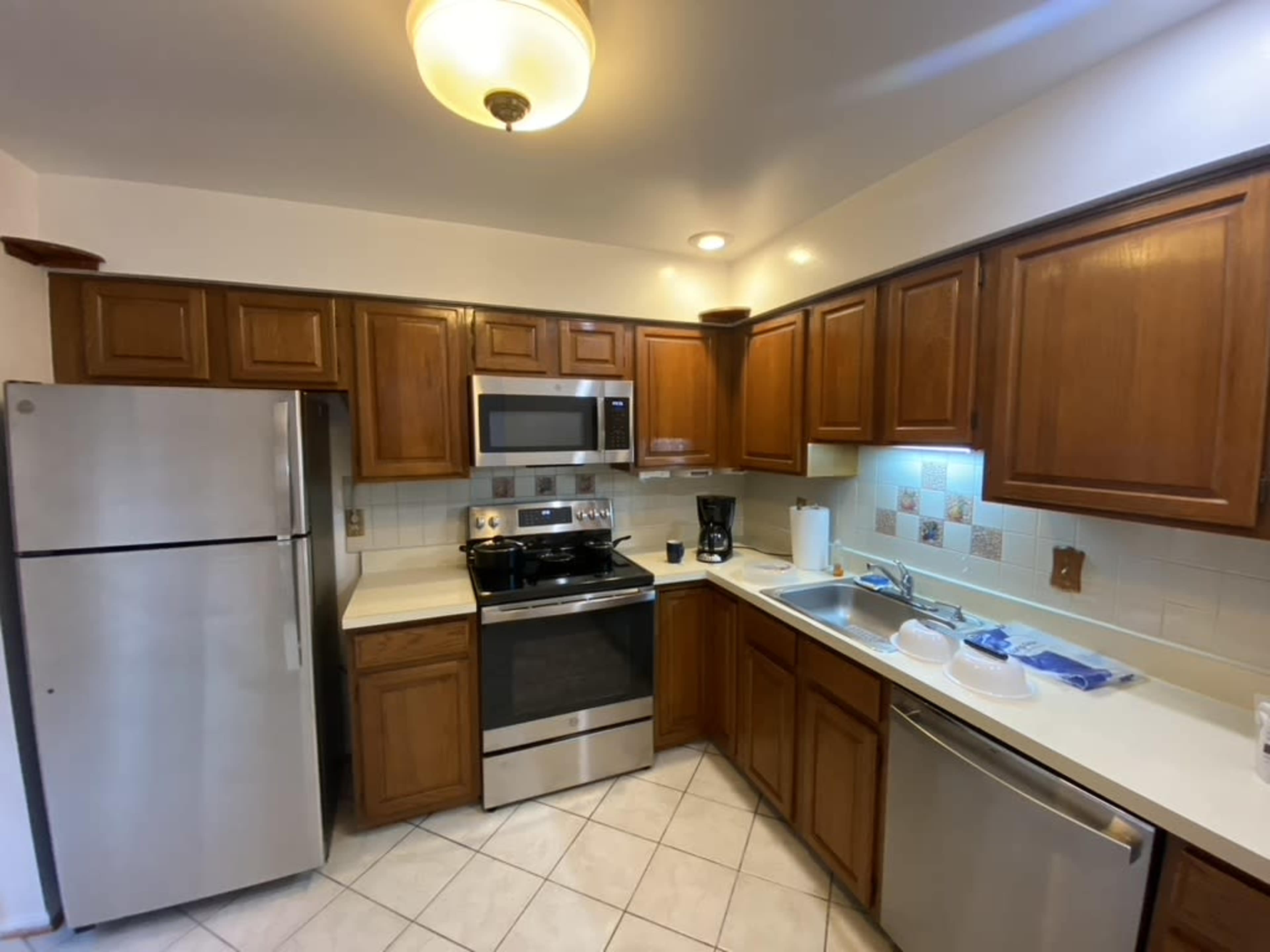 A kitchen featuring wooden cabinets, stainless steel appliances, a white countertop, and tiled flooring.