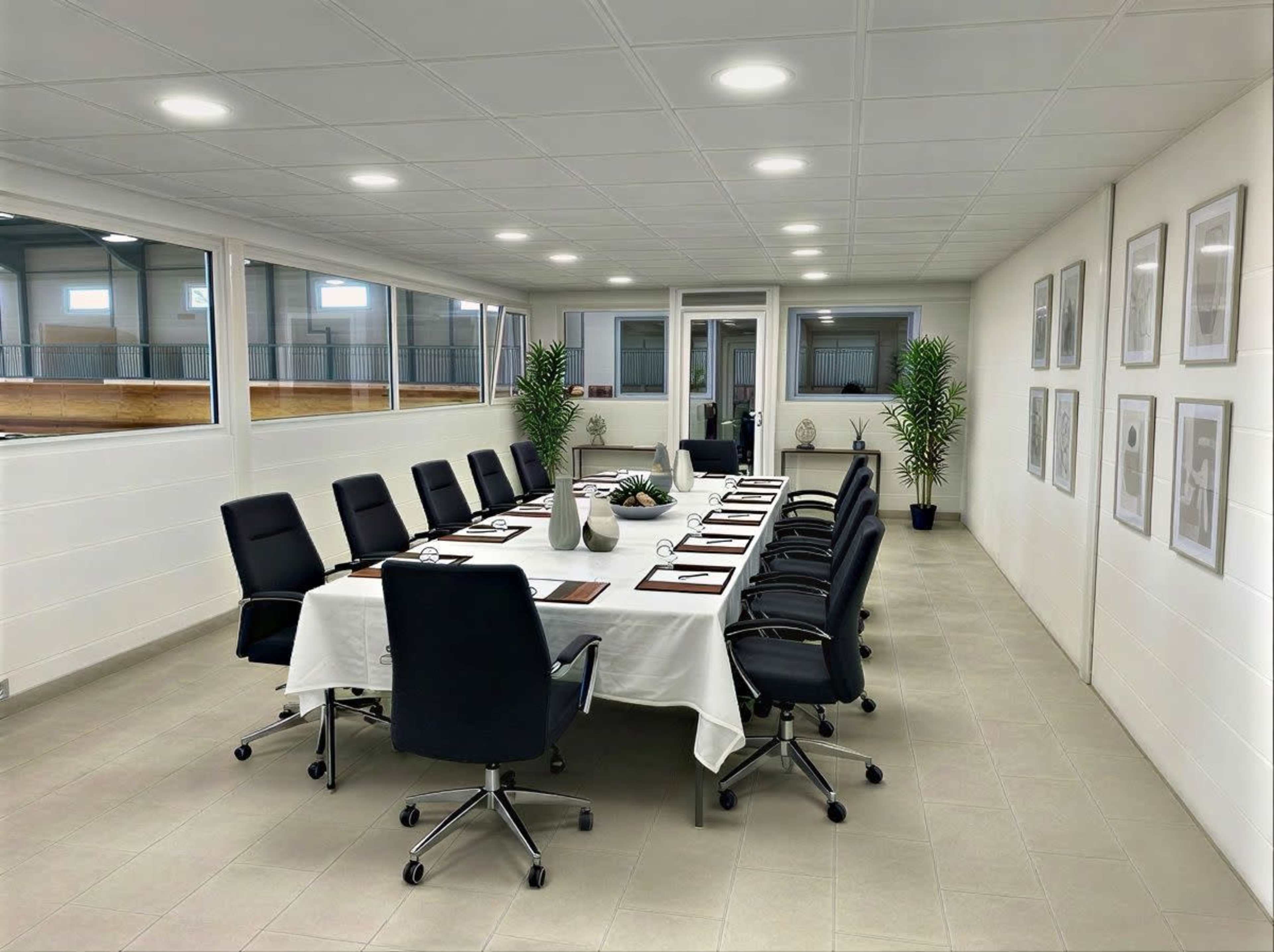 A large conference room features a long table set with place settings and surrounded by black chairs, with windows allowing natural light to illuminate the space.