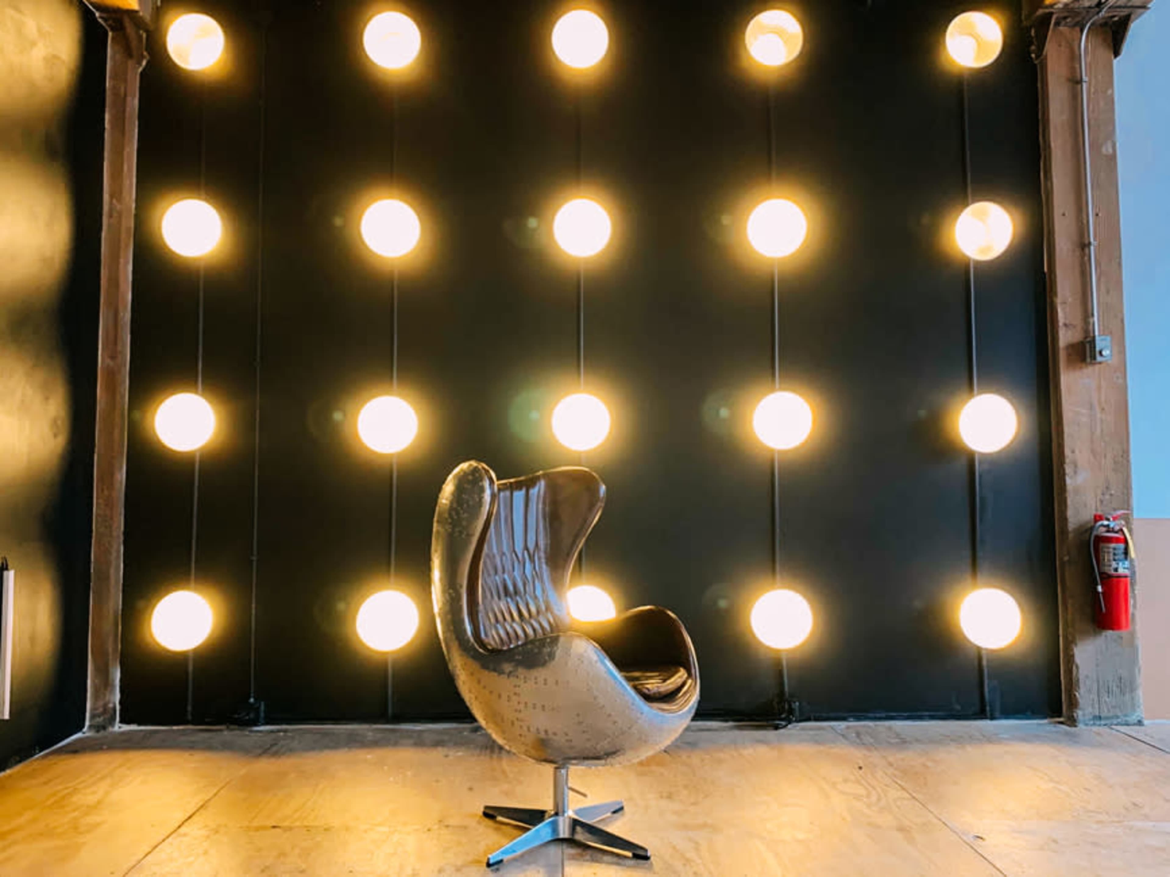 A modern chair is positioned in front of a wall illuminated by multiple spherical lights.