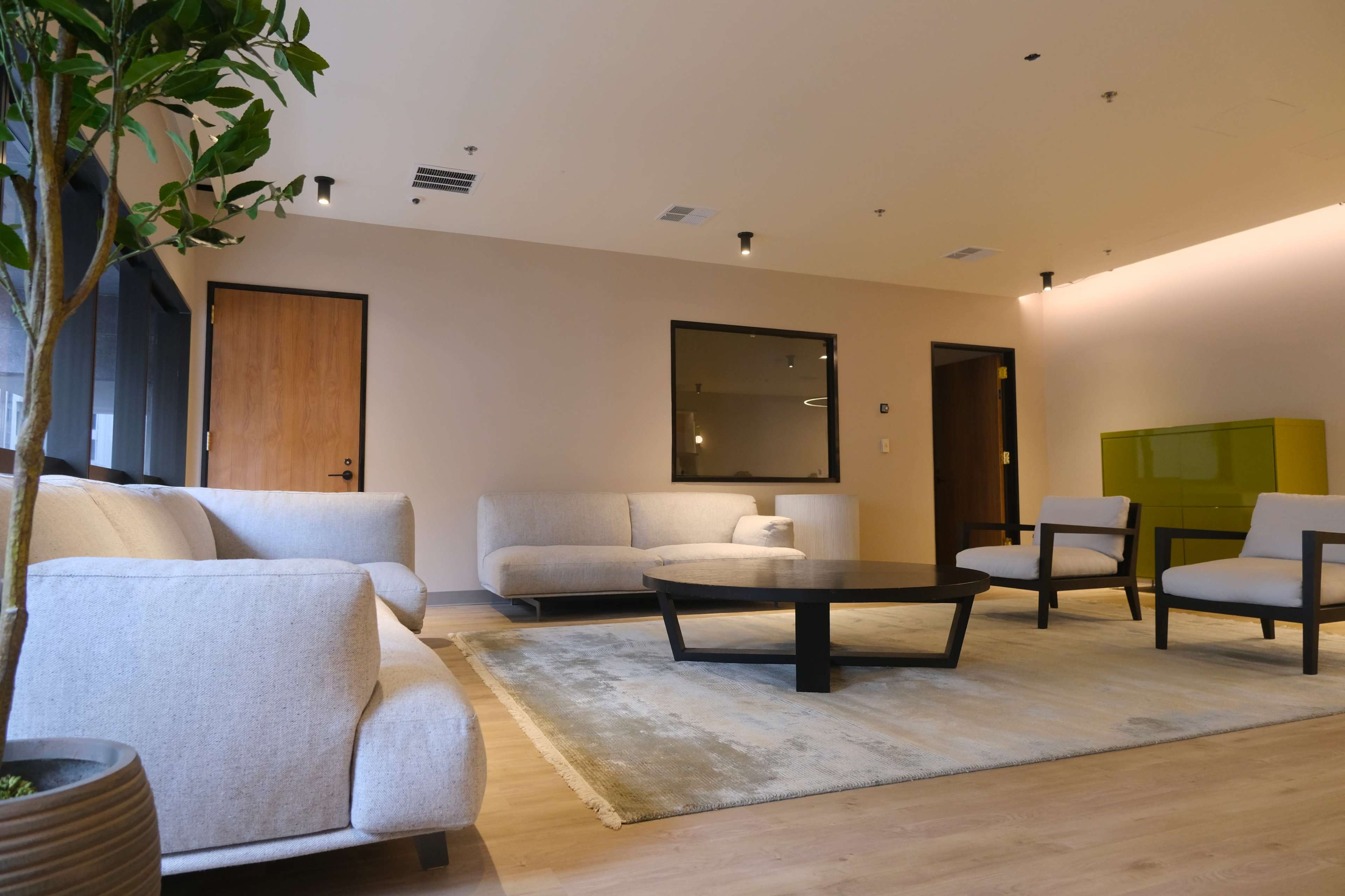 A modern lounge area with light-colored sofas, a circular coffee table, and a green cabinet against the wall.