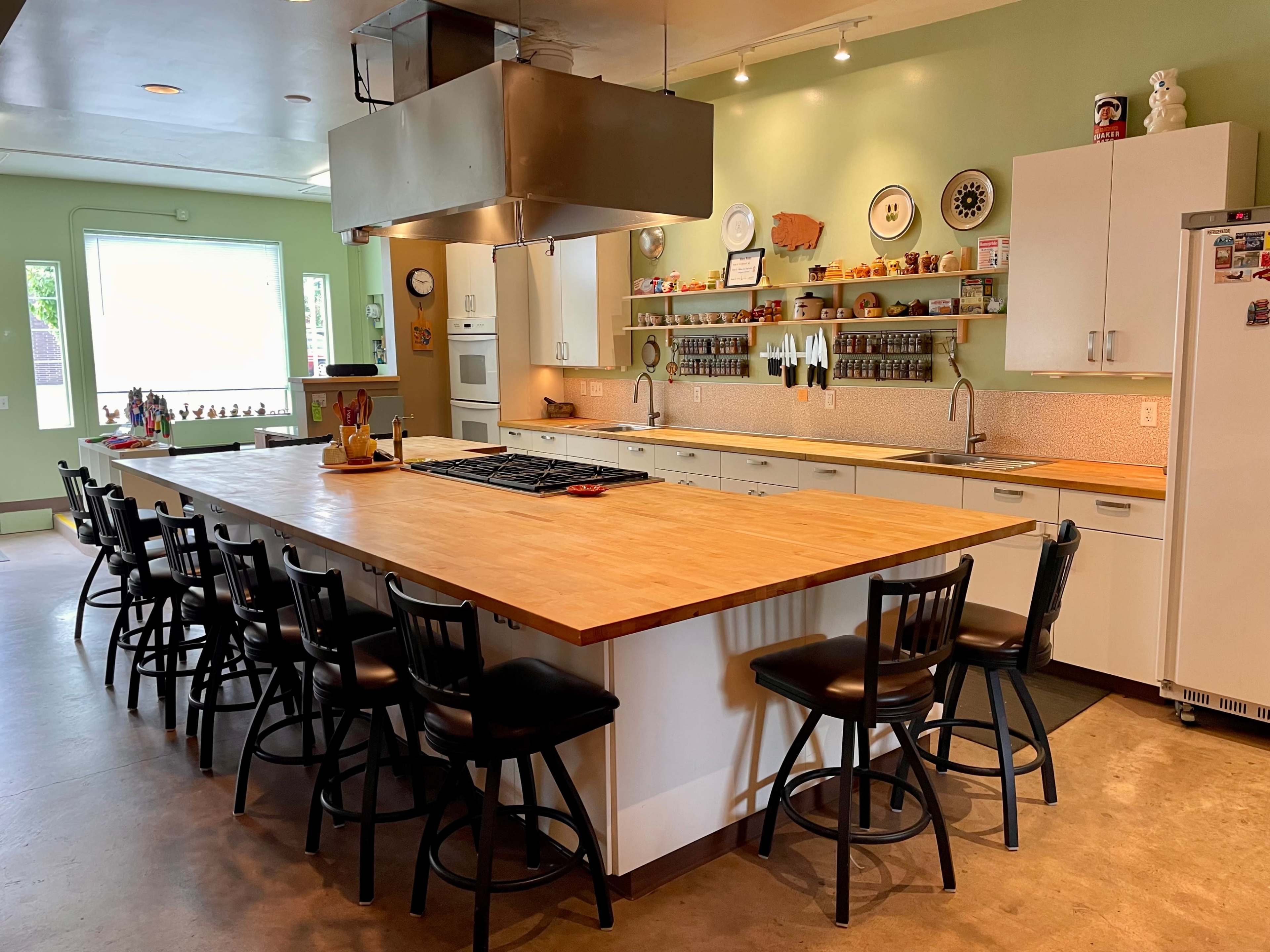 A spacious kitchen with a large central island, equipped with a stovetop, surrounded by black chairs and characterized by white cabinetry and green walls.