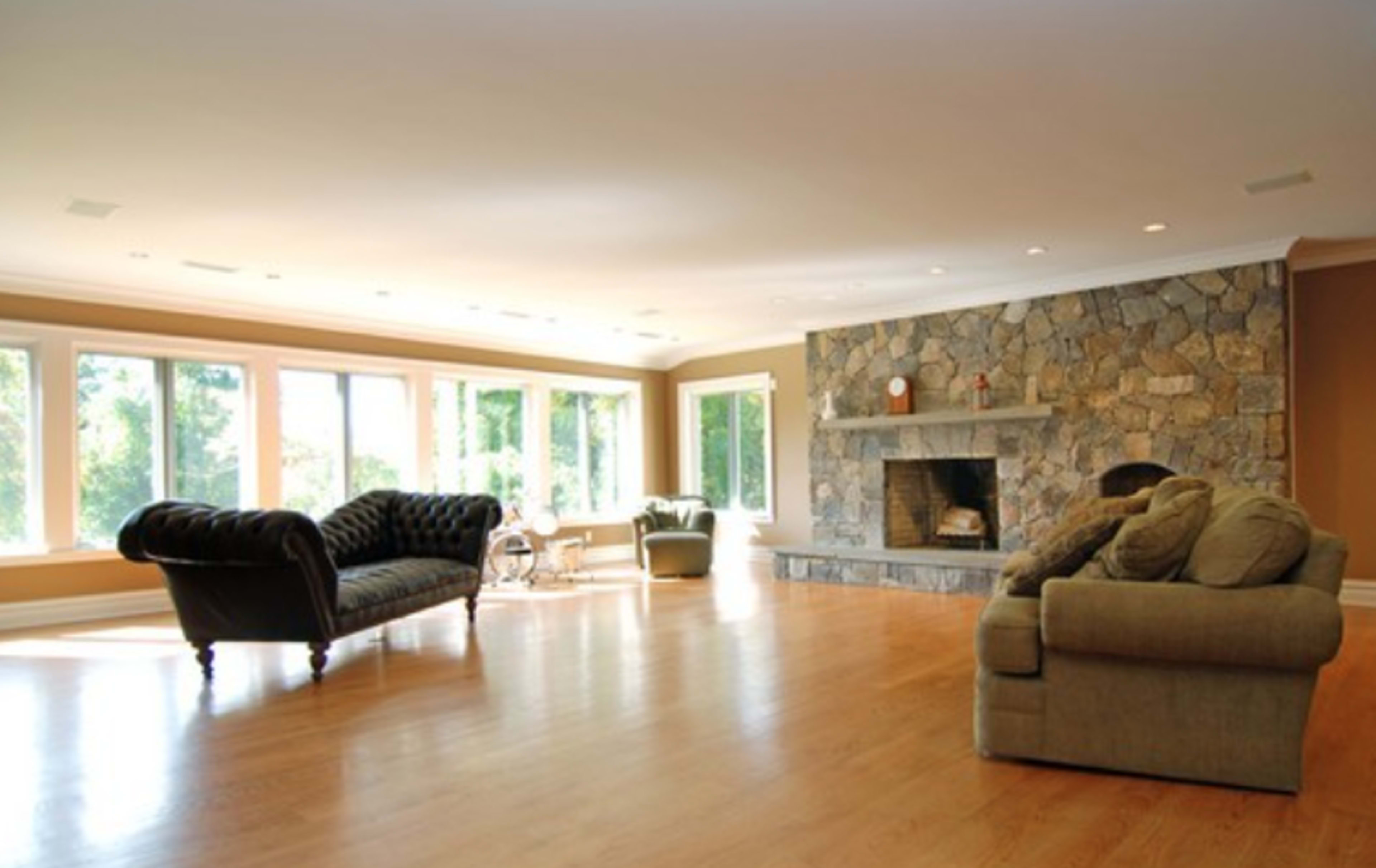 The spacious living room features large windows, a stone fireplace, and two sofas arranged on a hardwood floor.