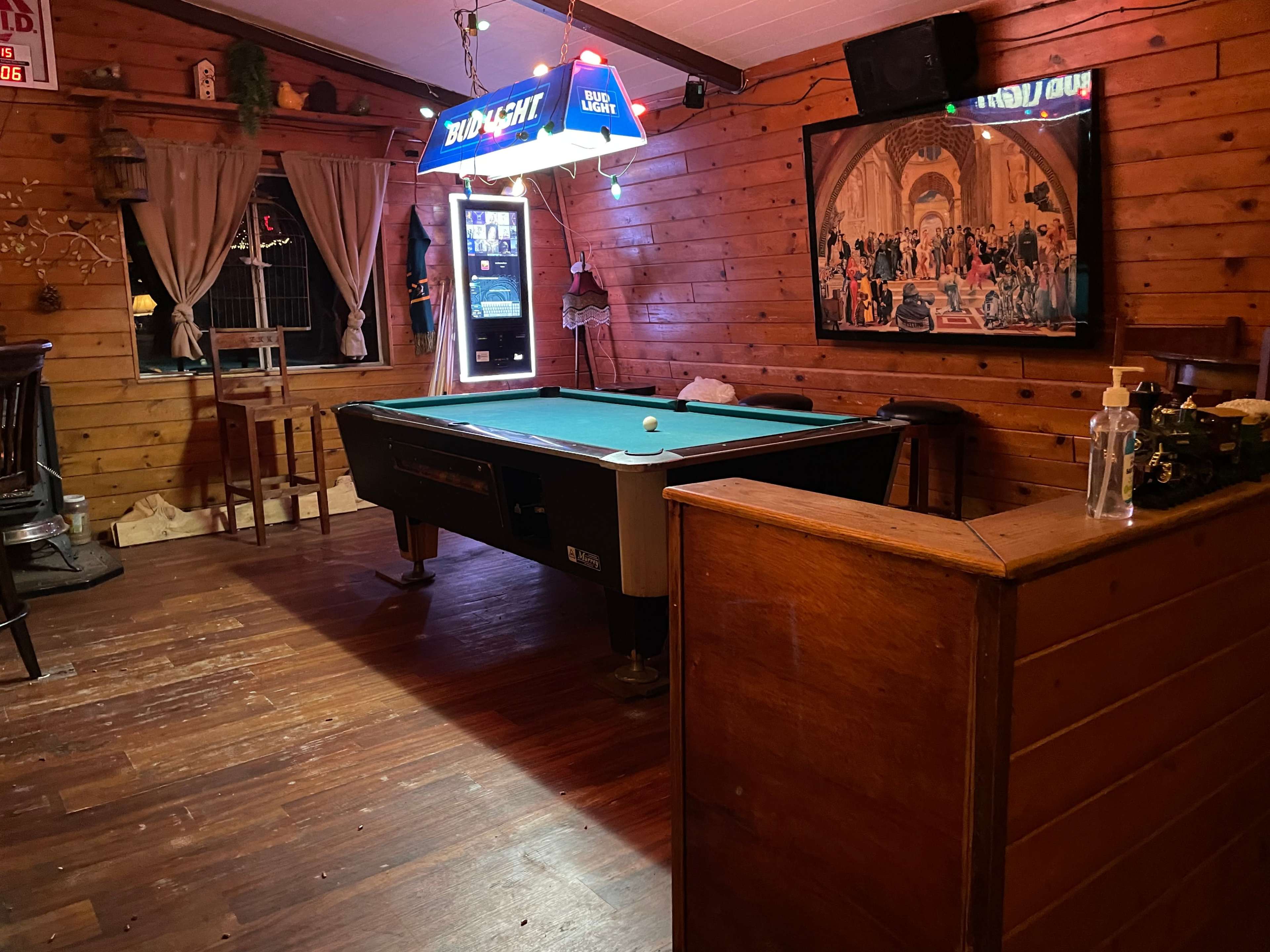 The image shows a wooden-paneled room with a pool table, a bar area, and a vintage-style illuminated sign.
