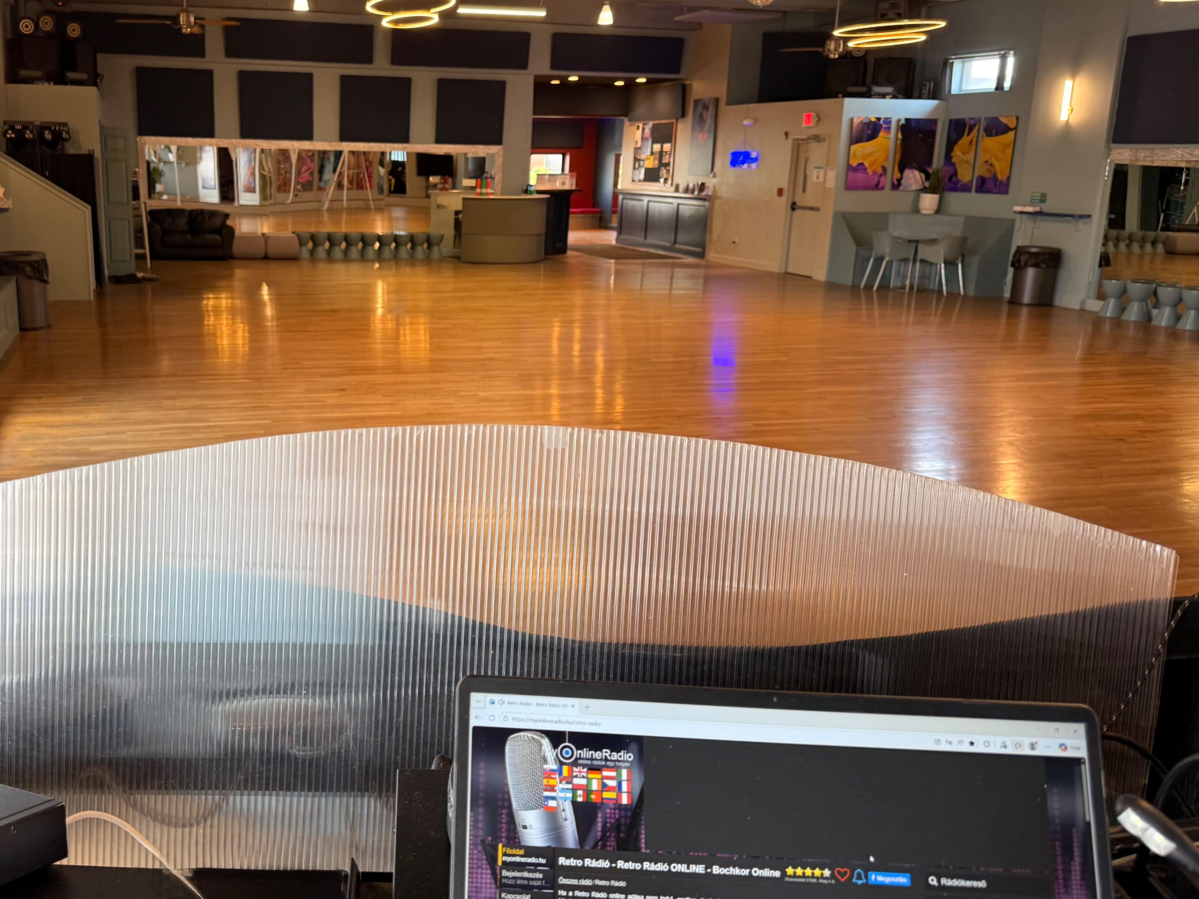 The image shows a spacious dance studio with polished wooden floors, large mirrors, and various seating areas in the background.
