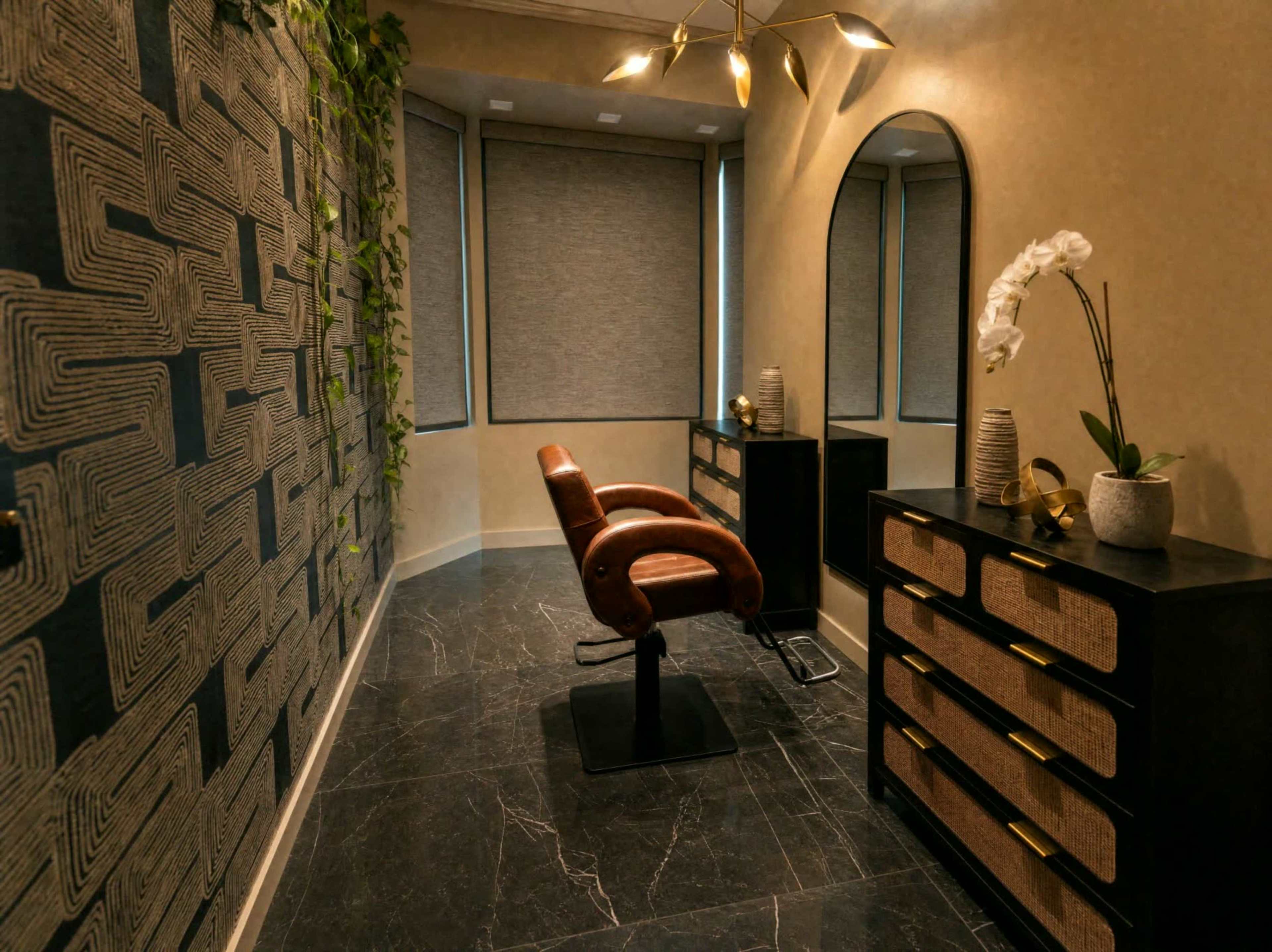 The image shows a modern salon interior featuring a styling chair, a mirror, and a dark dresser against a patterned wall, with plants and decorative items.