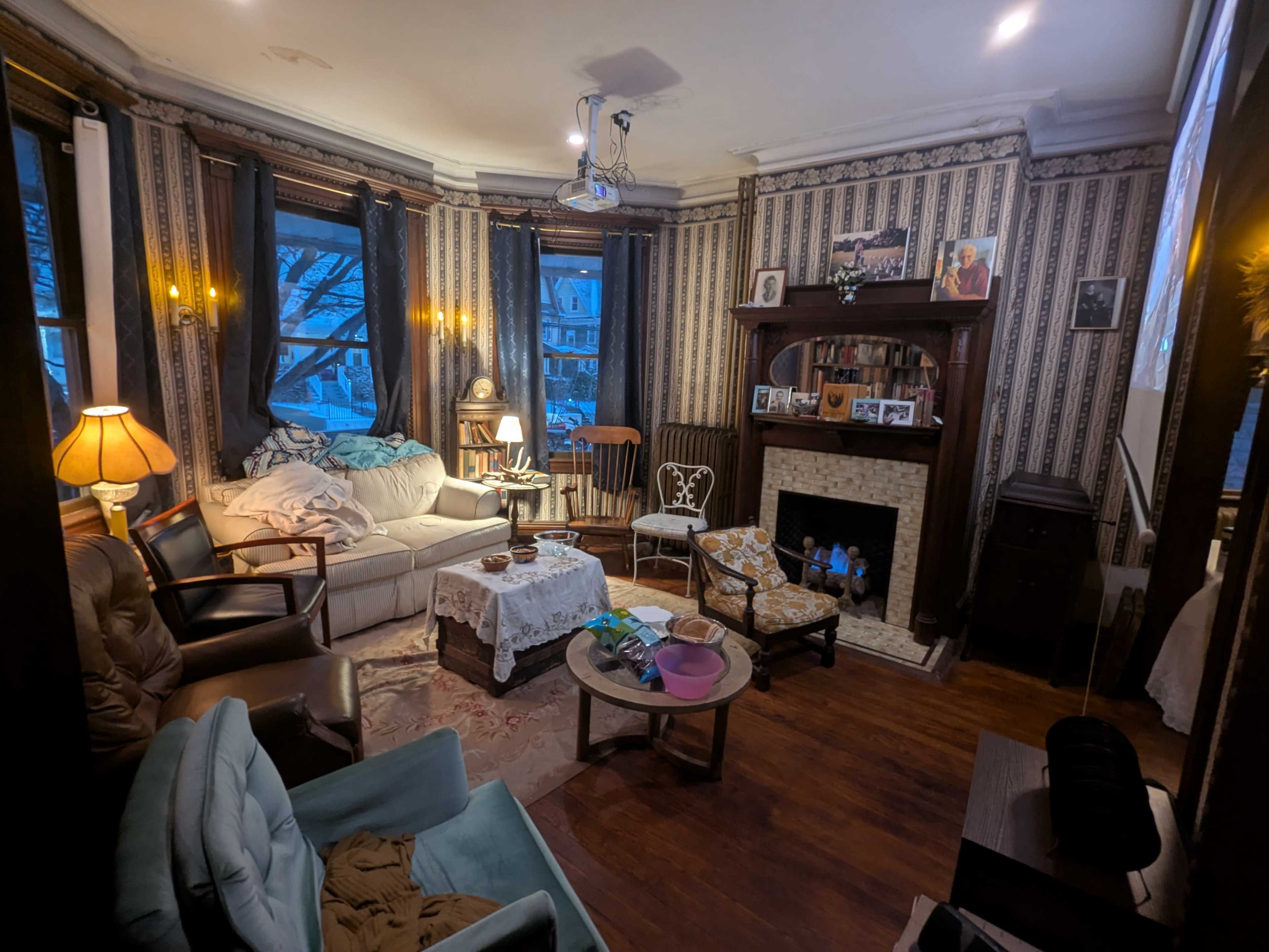 The room features a cozy living area with a mix of vintage furniture, including a sofa, armchairs, and a coffee table, all arranged around a fireplace.