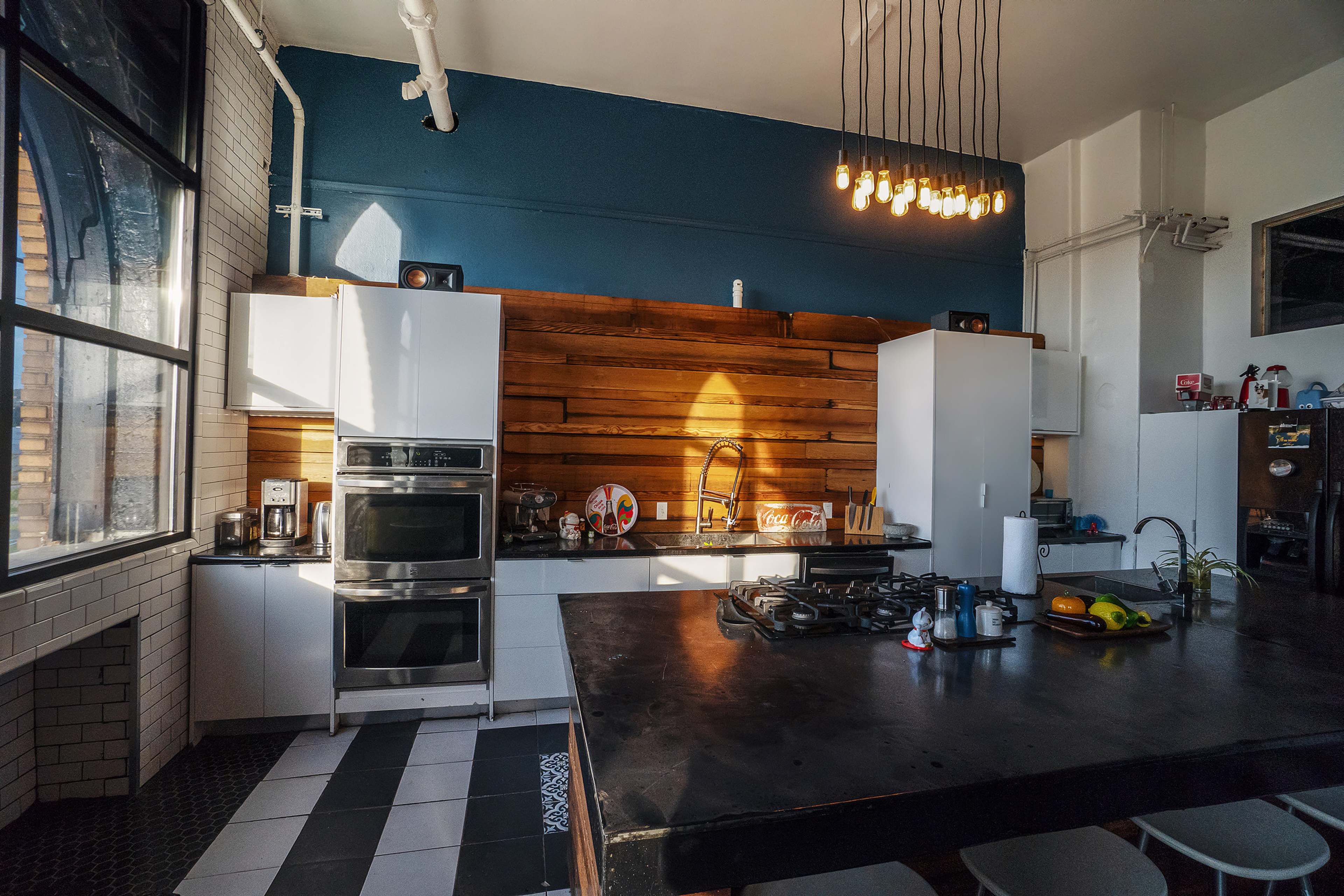 A modern kitchen features a dark wooden accent wall, white cabinetry, stainless steel appliances, and a large island with a black countertop.