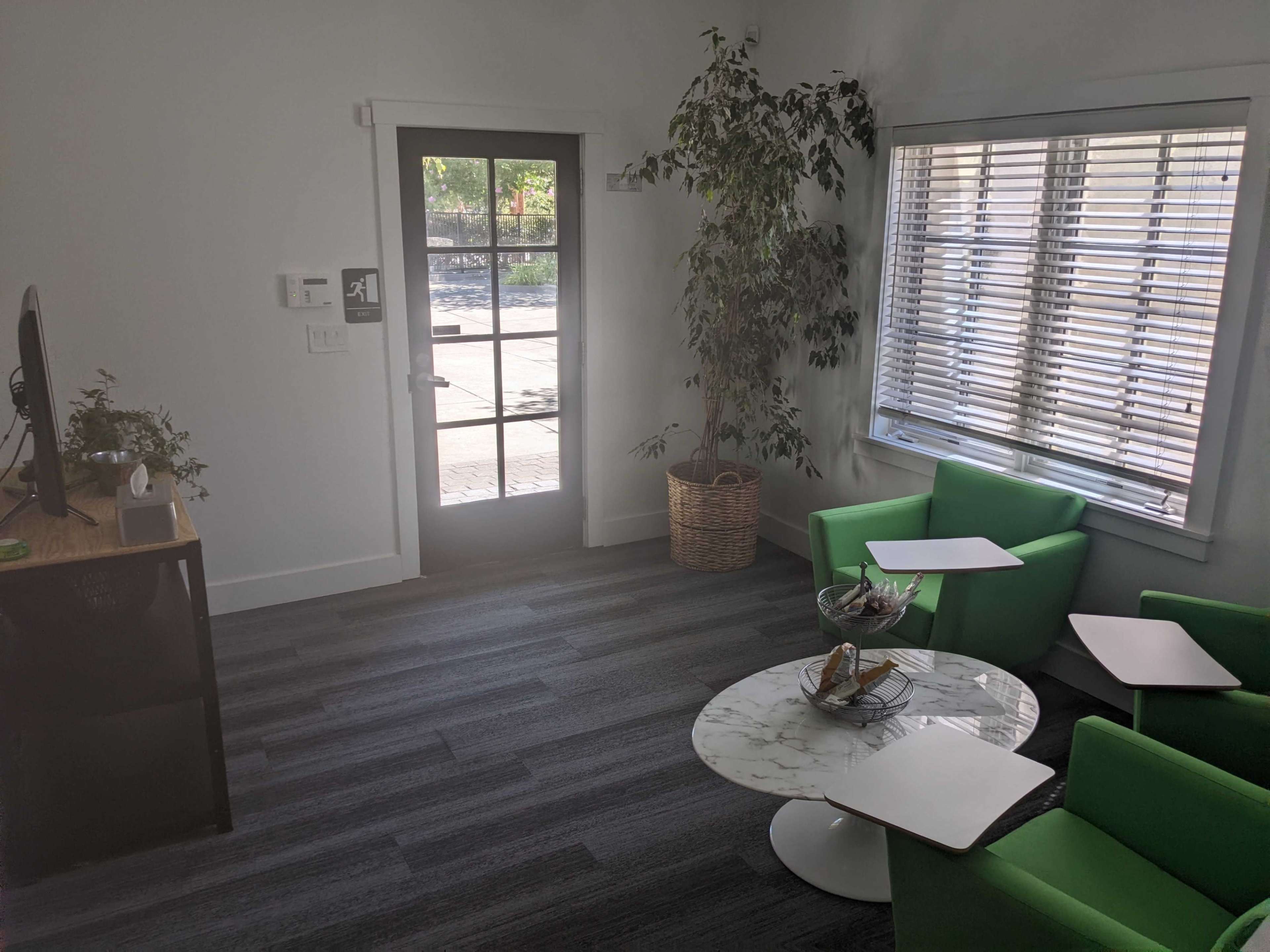 A bright, modern office space with green chairs, a marble coffee table, and a door leading to an outdoor area.