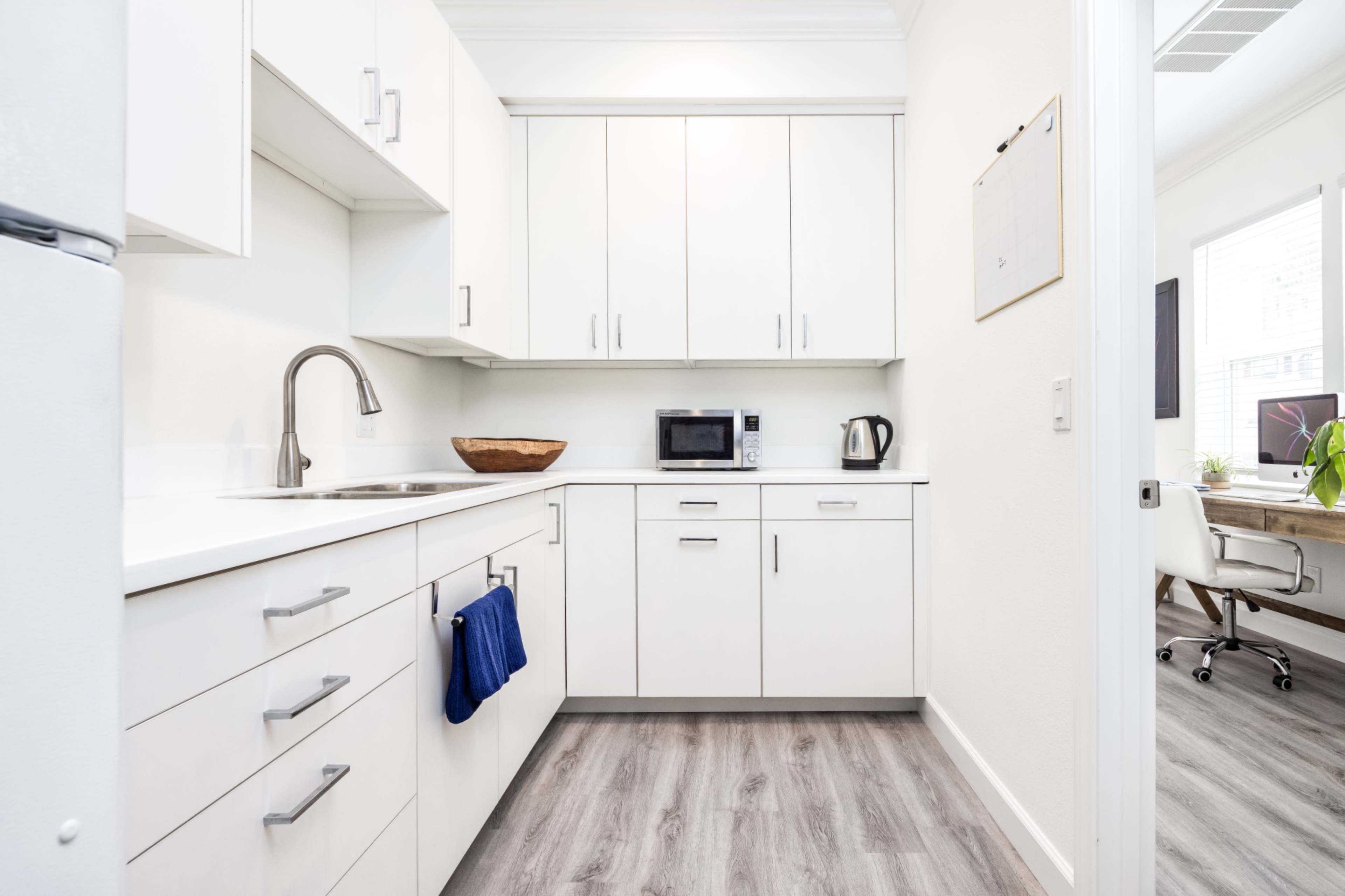 The image shows a modern kitchen with white cabinets, a sink, and appliances including a microwave and kettle.