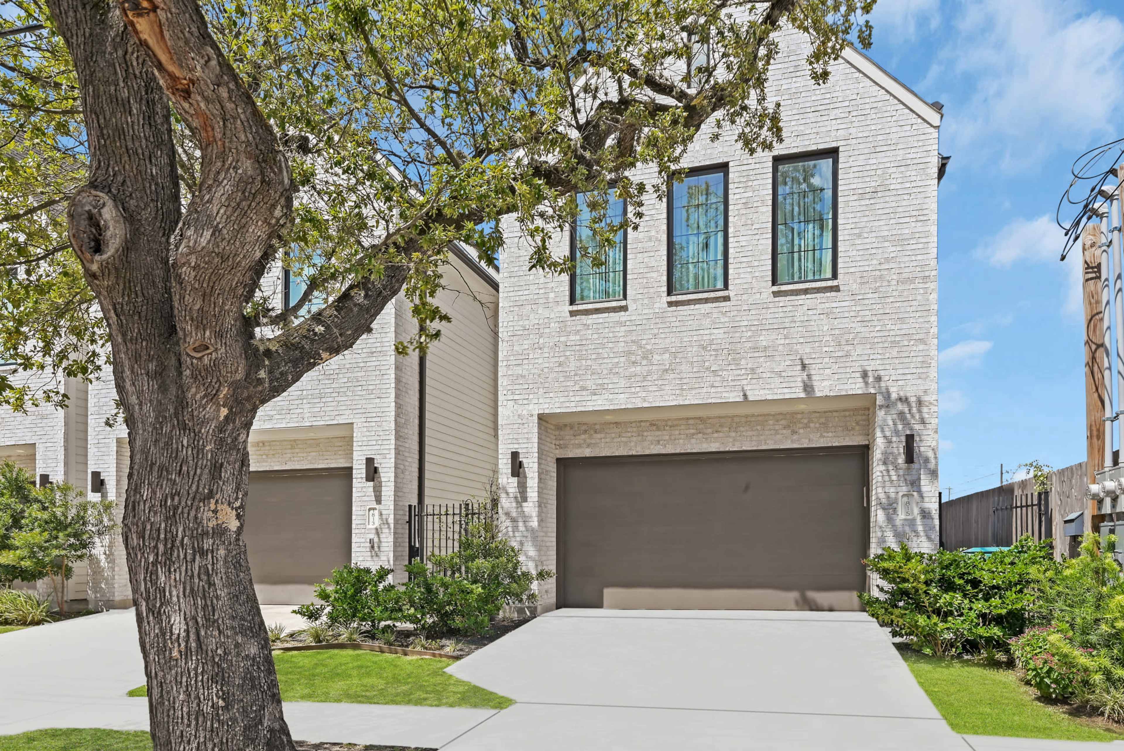 A modern two-story home with large windows and dark garage doors is set alongside a well-maintained lawn and a nearby tree.