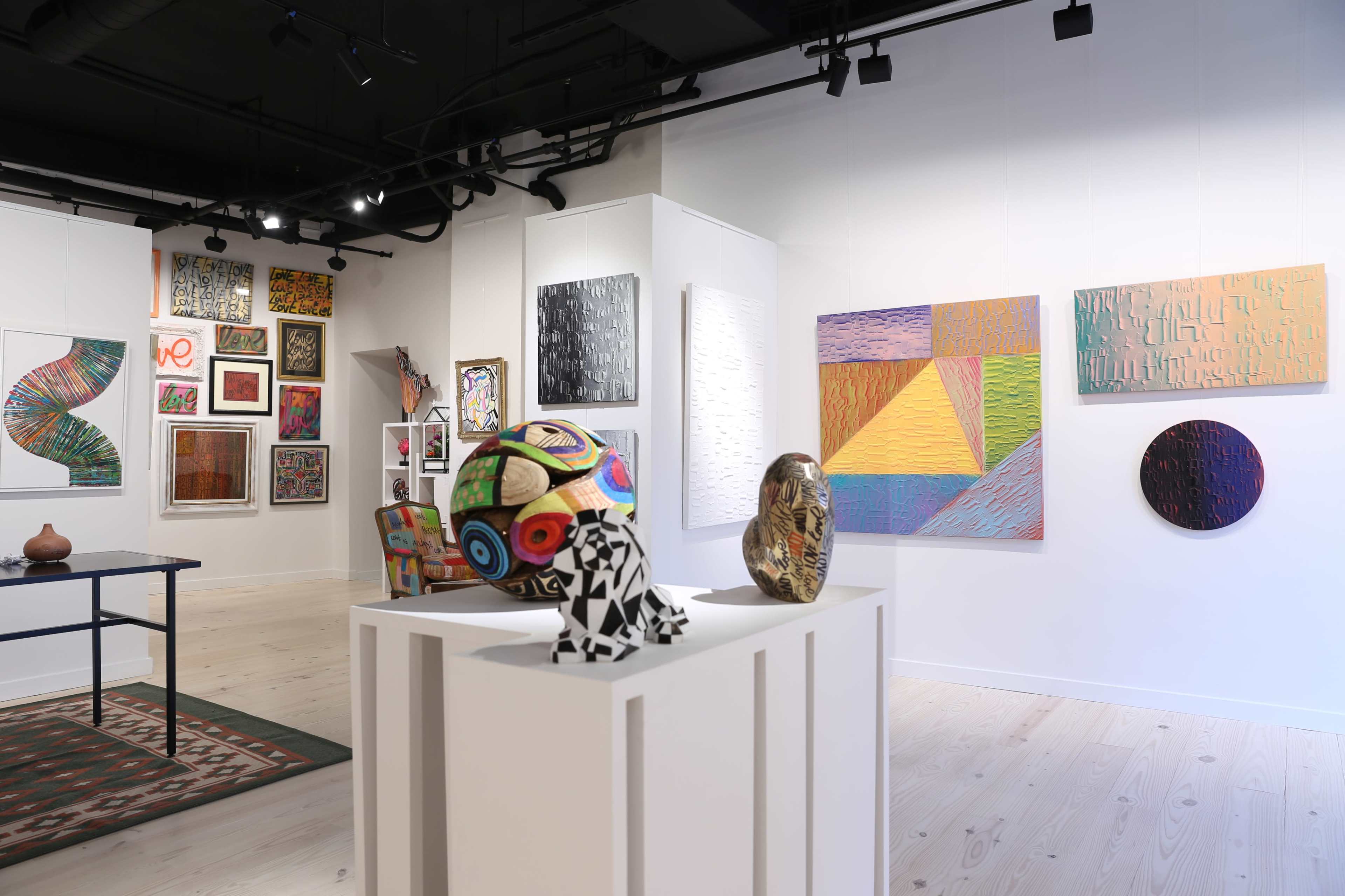 An art gallery displaying various colorful paintings and sculptures on white walls.