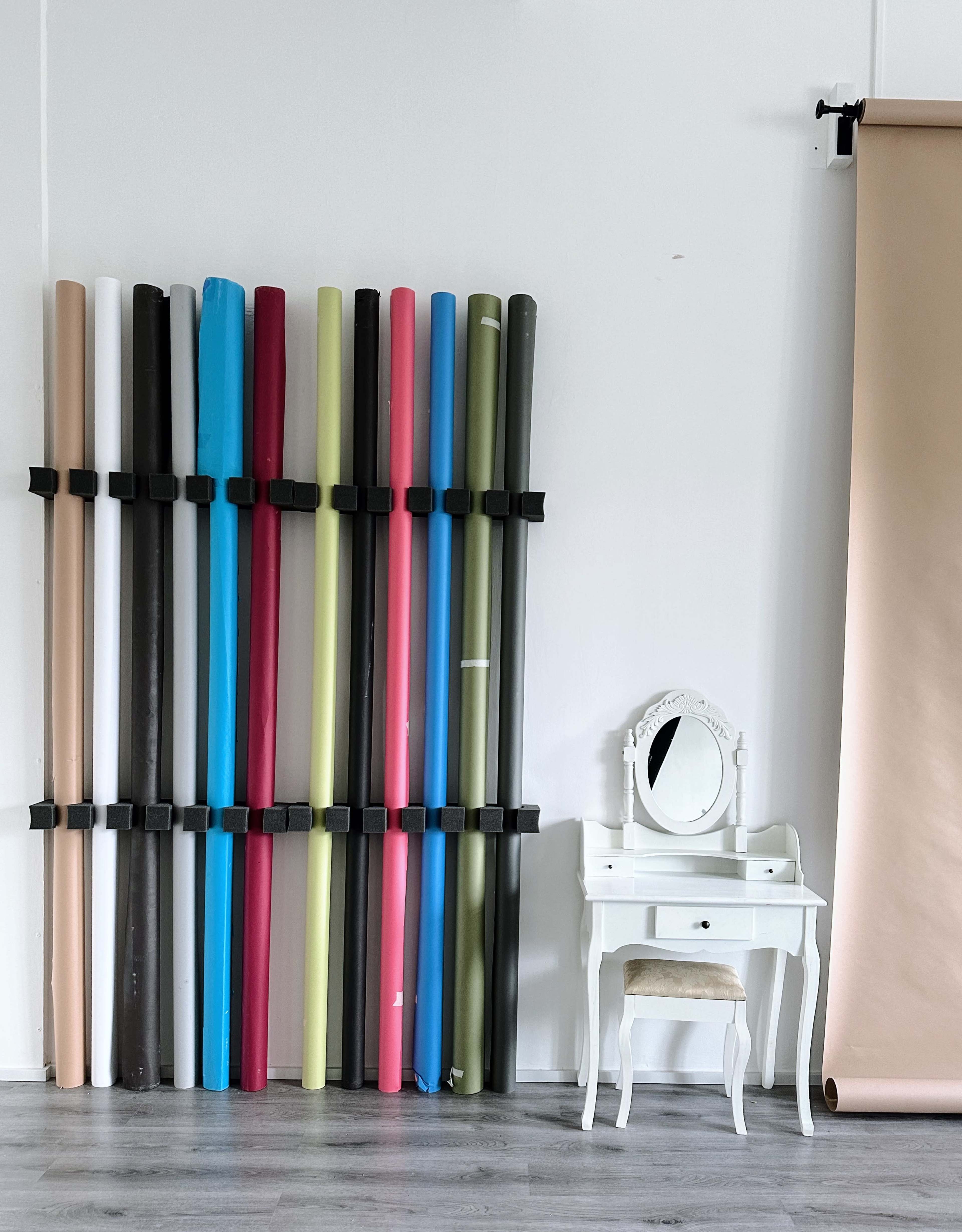 A wall-mounted arrangement of colored backdrop rolls next to a white vanity table with a round mirror.