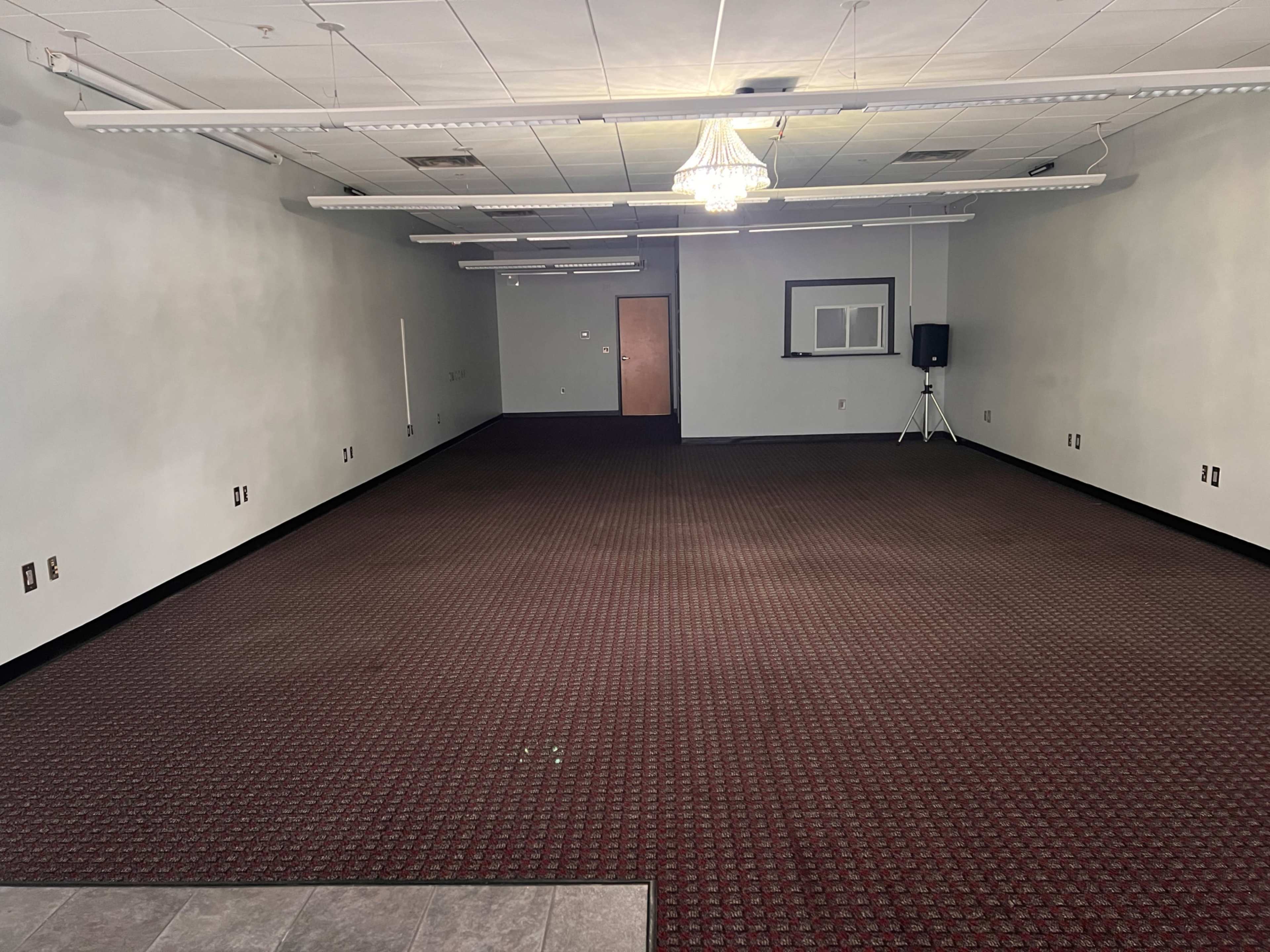 An empty room with a carpeted floor, walls painted in a light color, and a chandelier hanging from the ceiling.