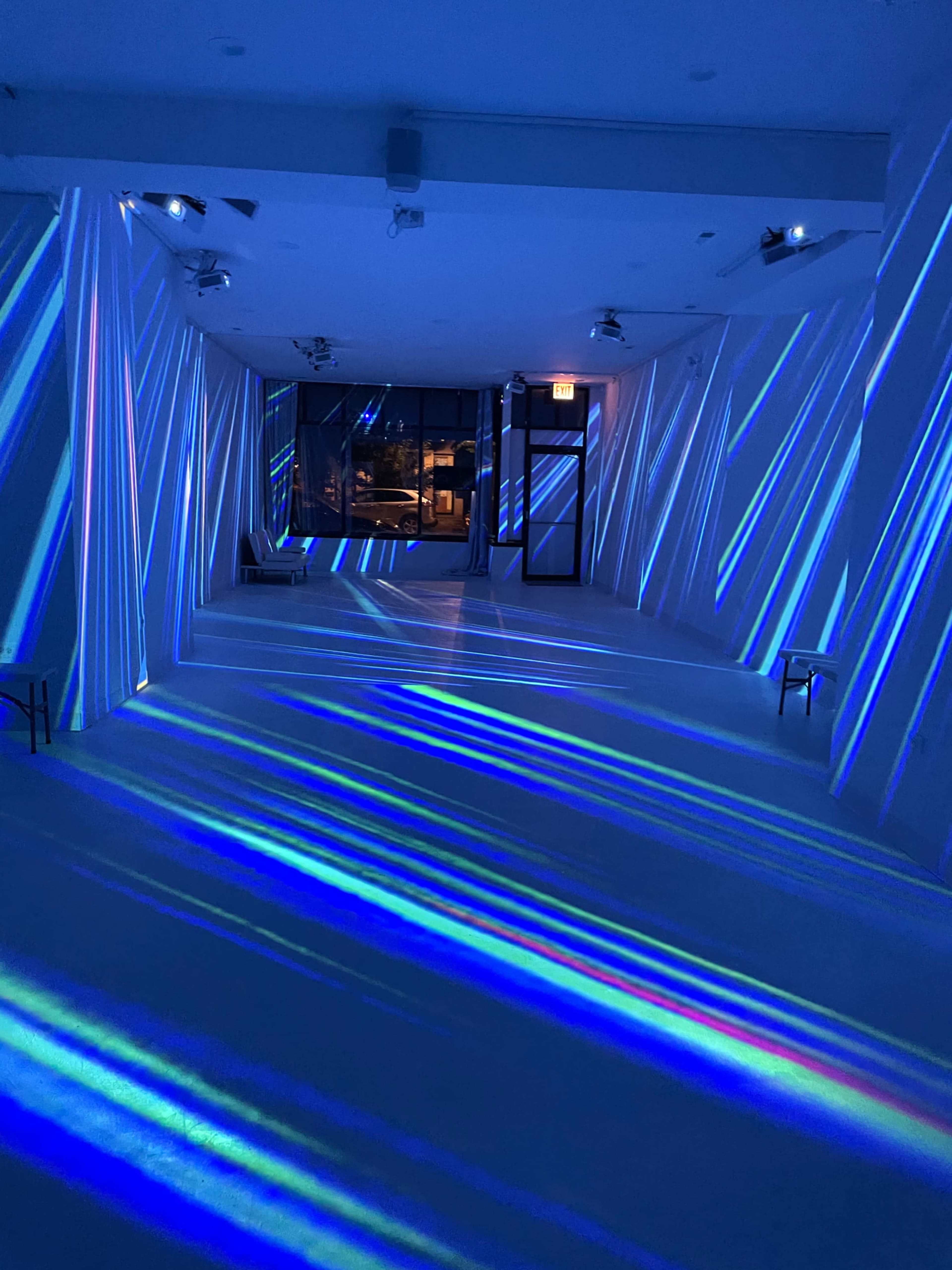 A spacious gallery with blue and white light projections creating diagonal patterns across the walls and floor.