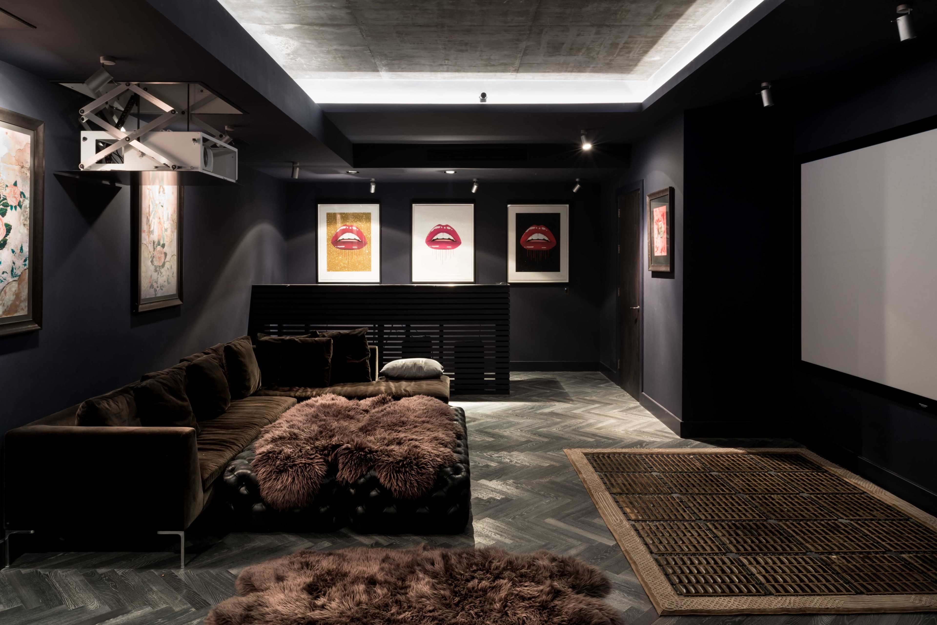 The image features a dimly lit modern lounge with a plush sofa, artwork on the walls, and a large screen for viewing.