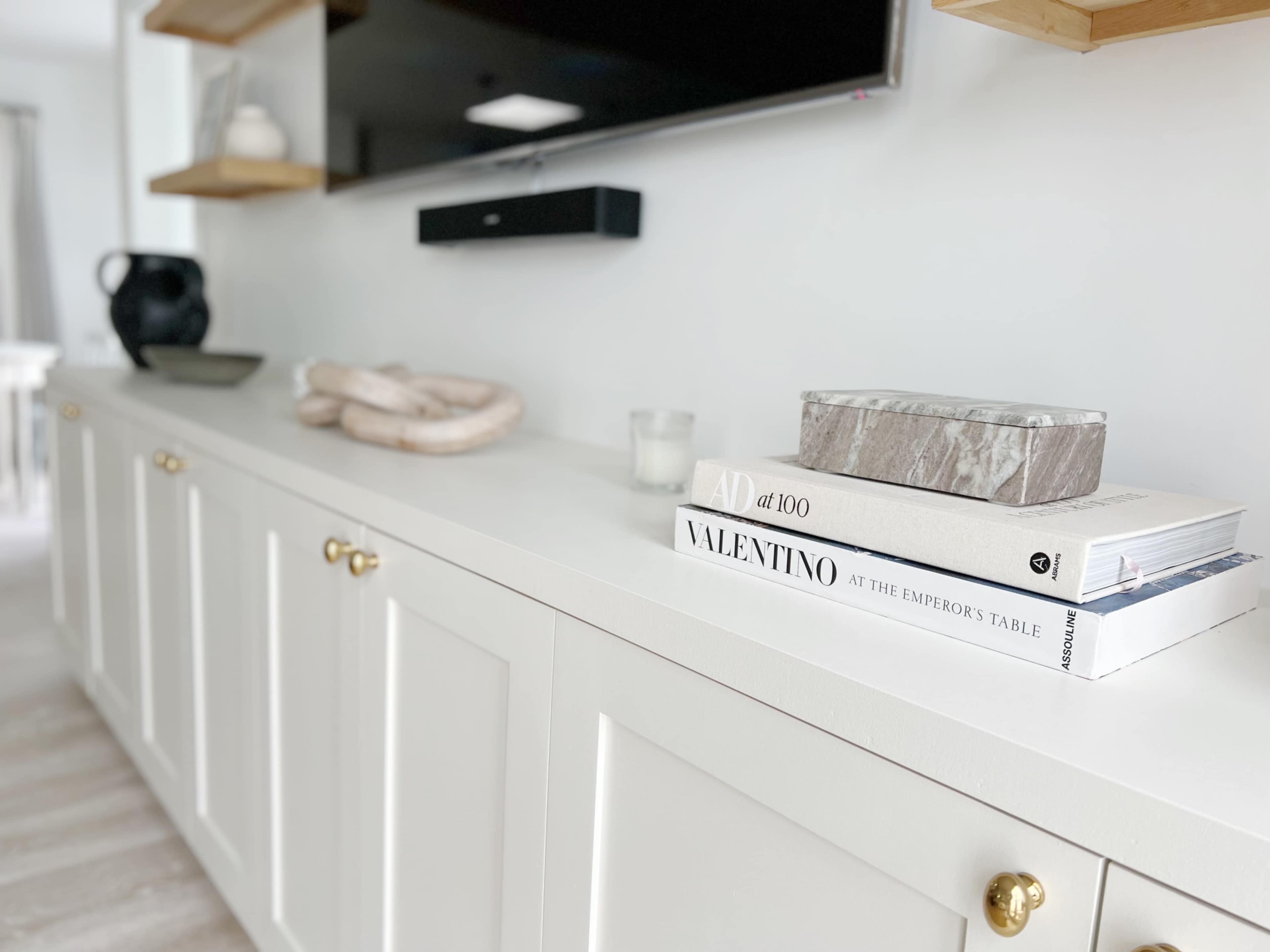 A modern white sideboard showcases a selection of decorative books and a small marble box, with a television mounted above it.