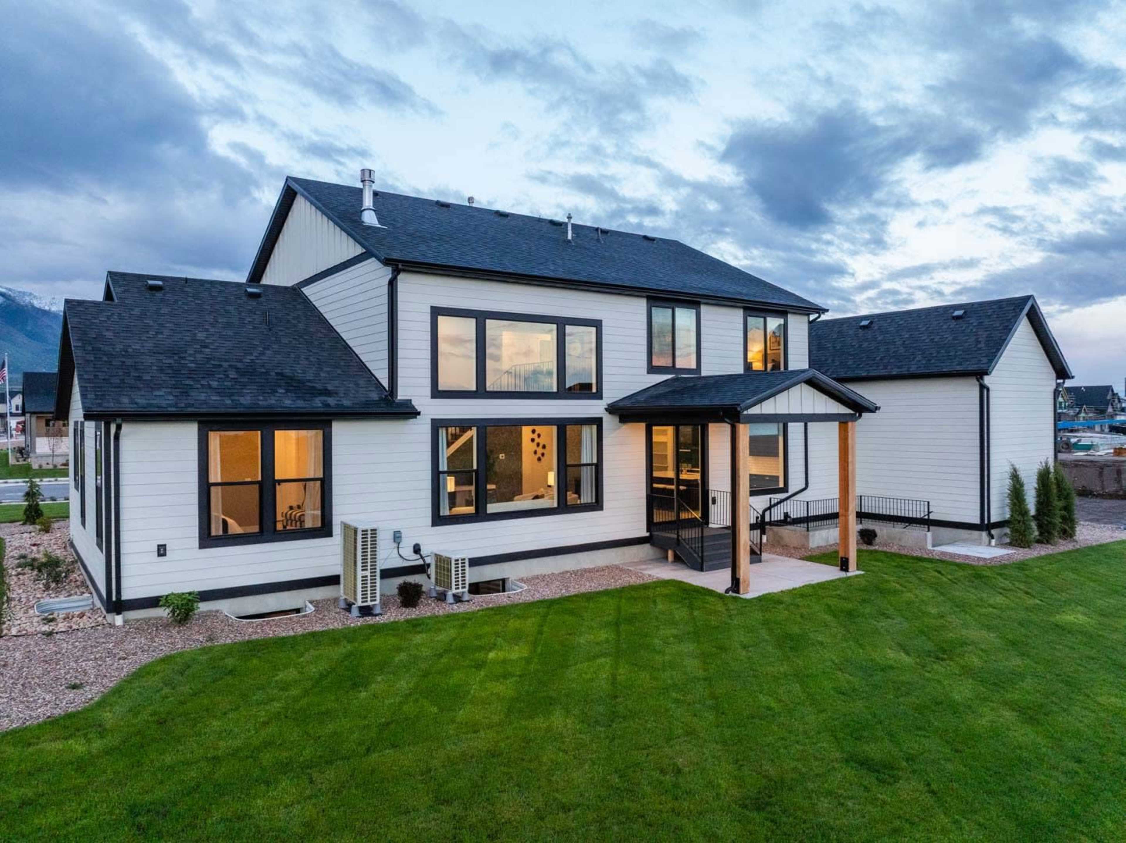 A modern two-story house with large windows, a covered entrance, and a well-maintained lawn is situated in an open area.