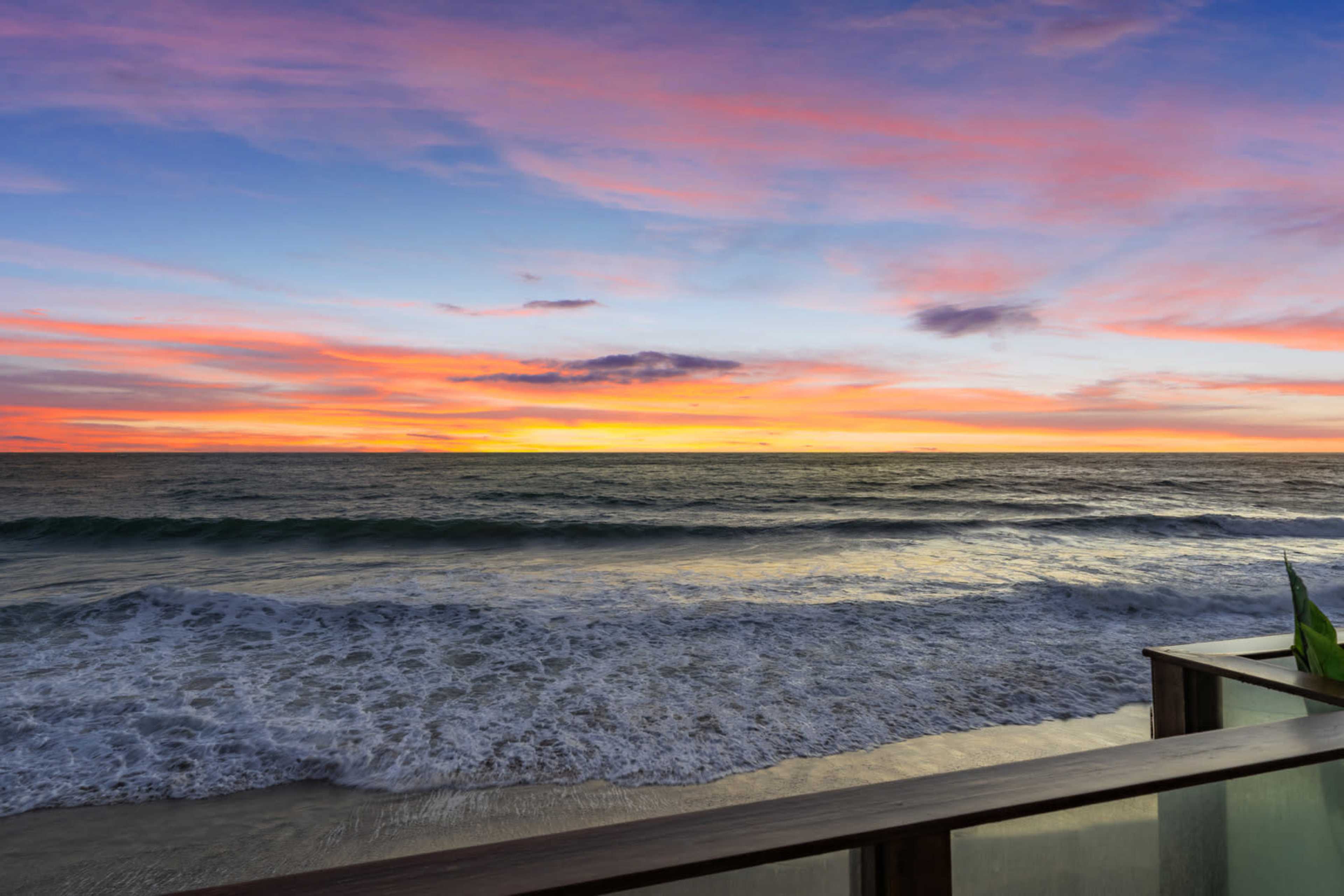 The image depicts a vibrant sunset over the ocean with waves gently rolling onto a sandy shore.