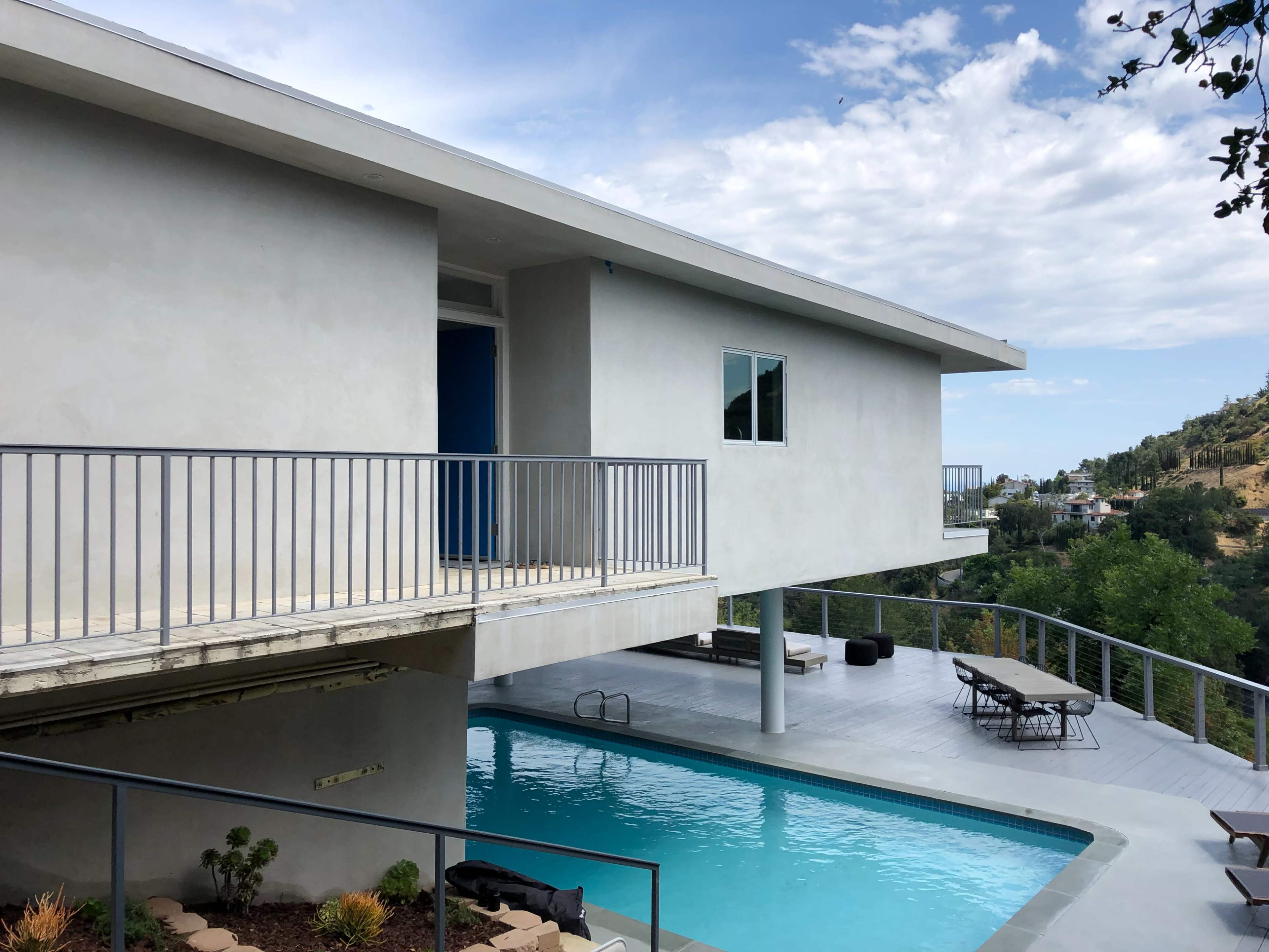 A modern two-story house with a swimming pool and a balcony overlooks a hillside landscape.