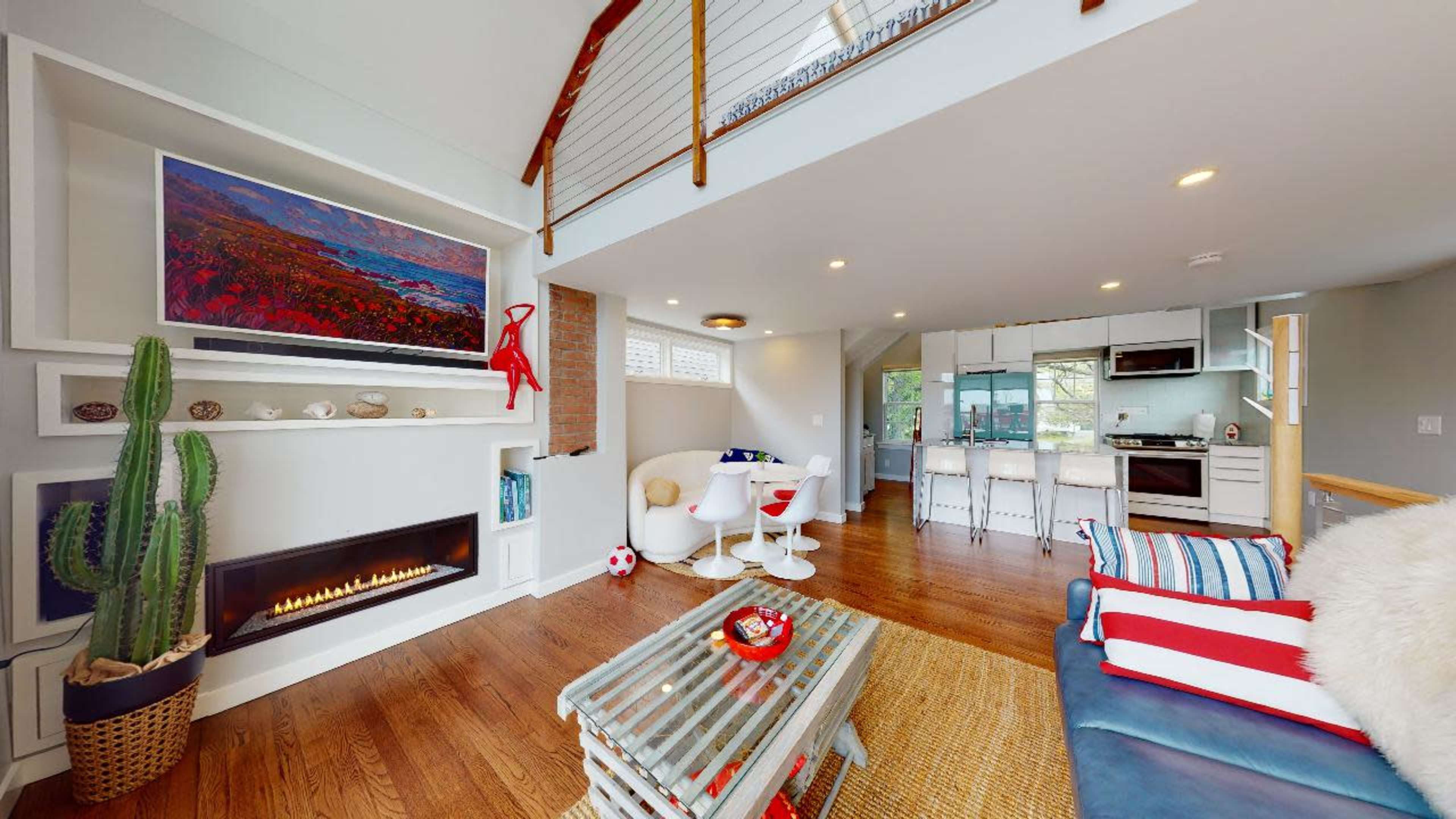 A modern living space featuring a fireplace, a large television mounted on the wall, and an open kitchen area with a dining space.