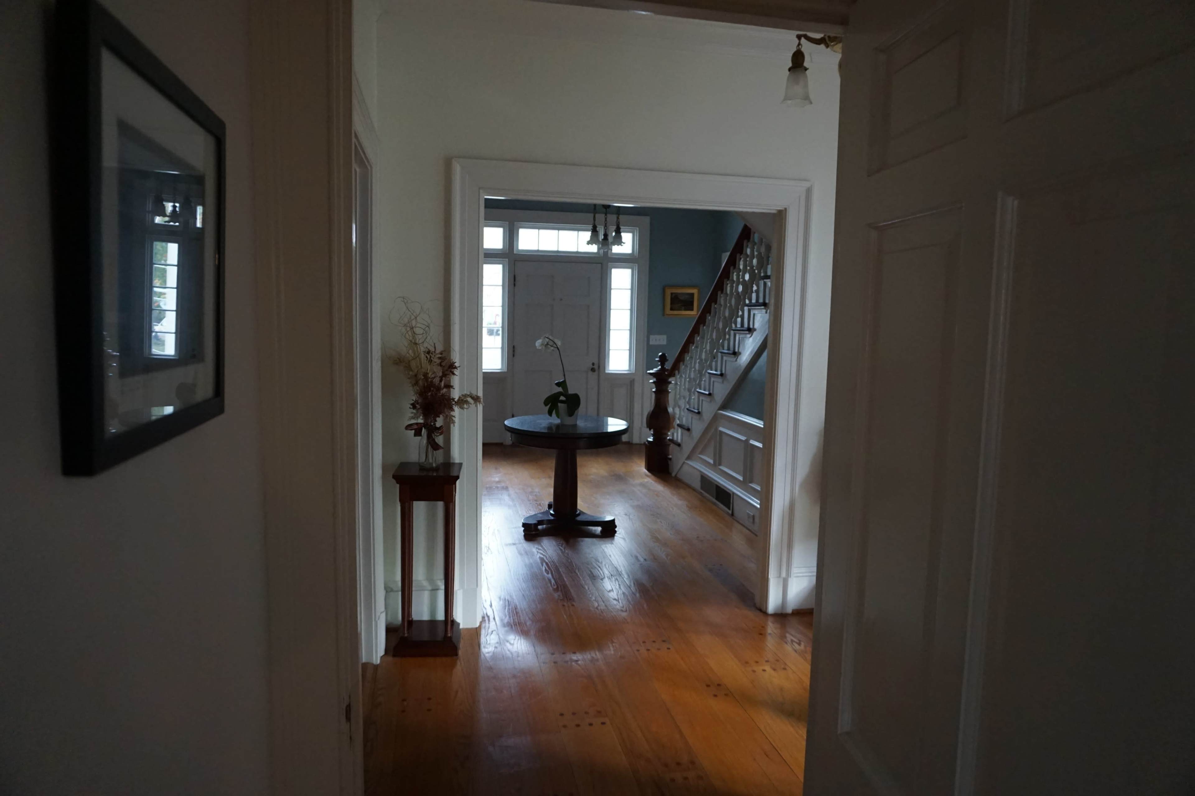 A hallway leads to a spacious room with a table in the center and a staircase on the right.