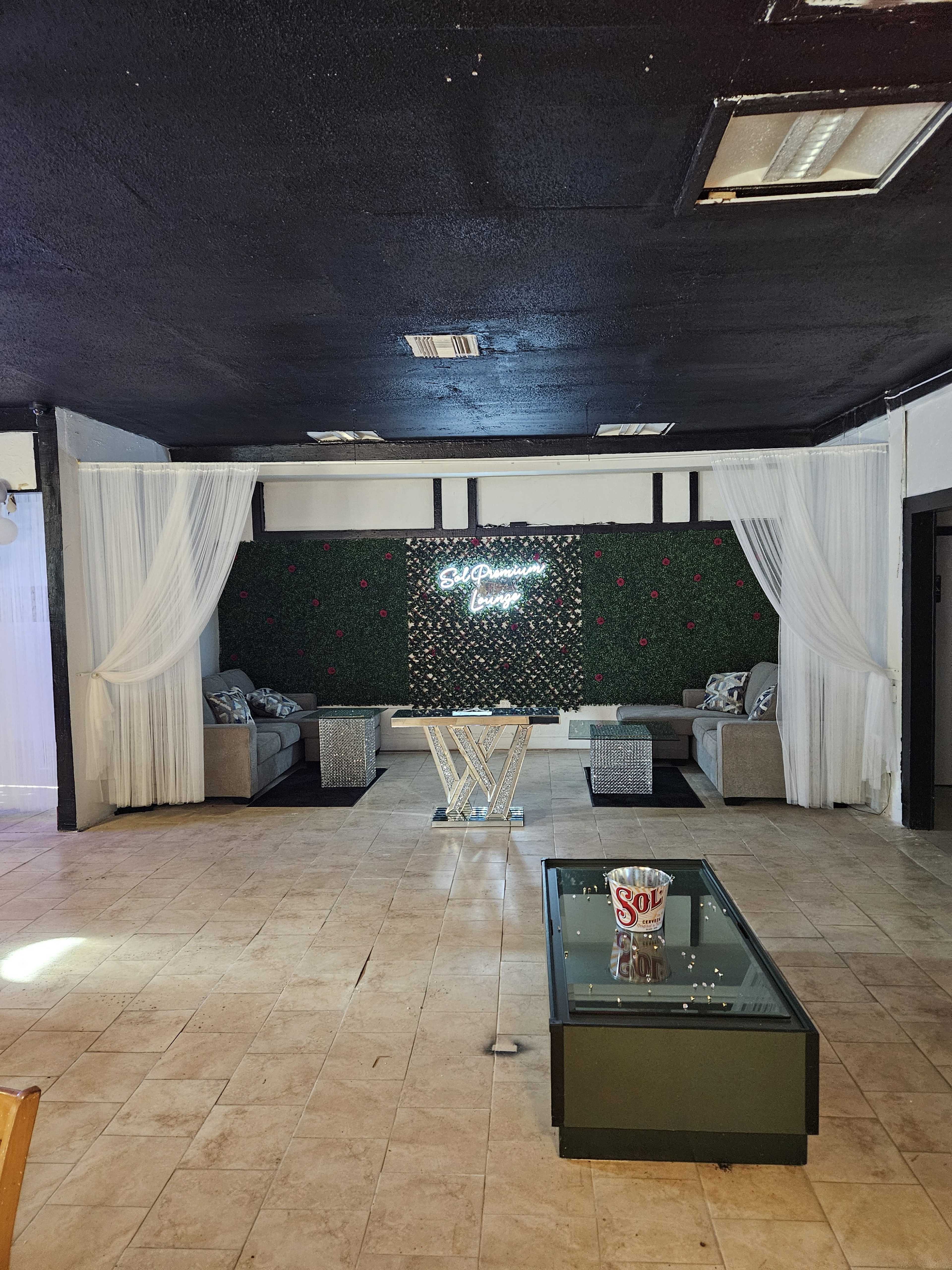 A seating area is arranged with two sofas and a glass table, illuminated by a neon sign in a room with a dark ceiling and decorated walls.
