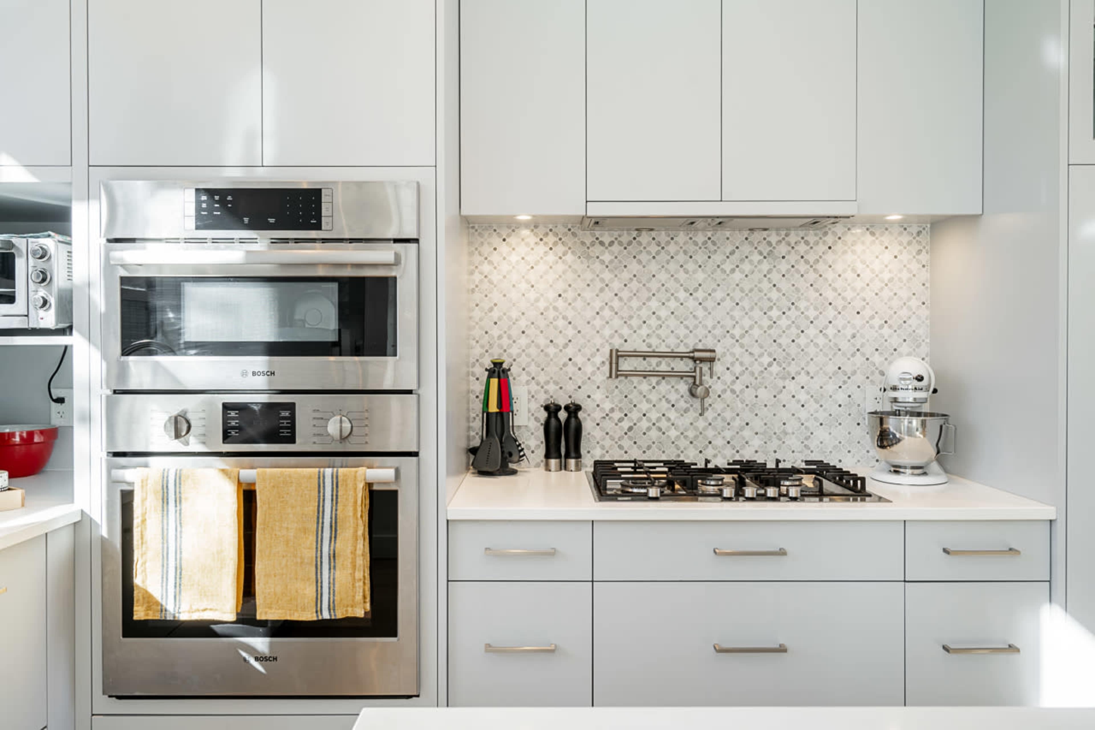 The kitchen features a modern design with stainless steel appliances, a marble backsplash, and gray cabinetry.