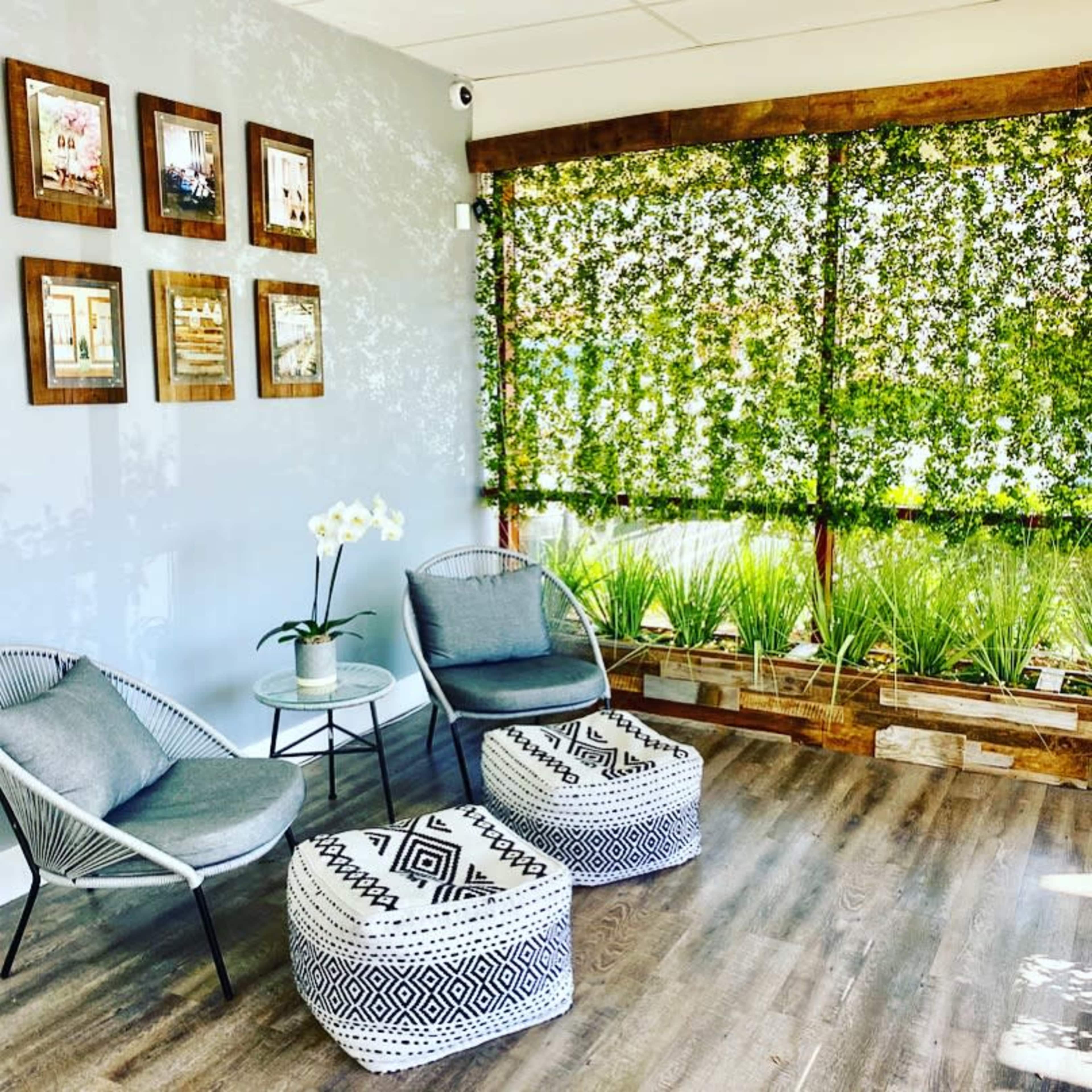 A cozy interior space featuring two chairs, a small table, and decorative plants partially obscured by a green privacy screen.