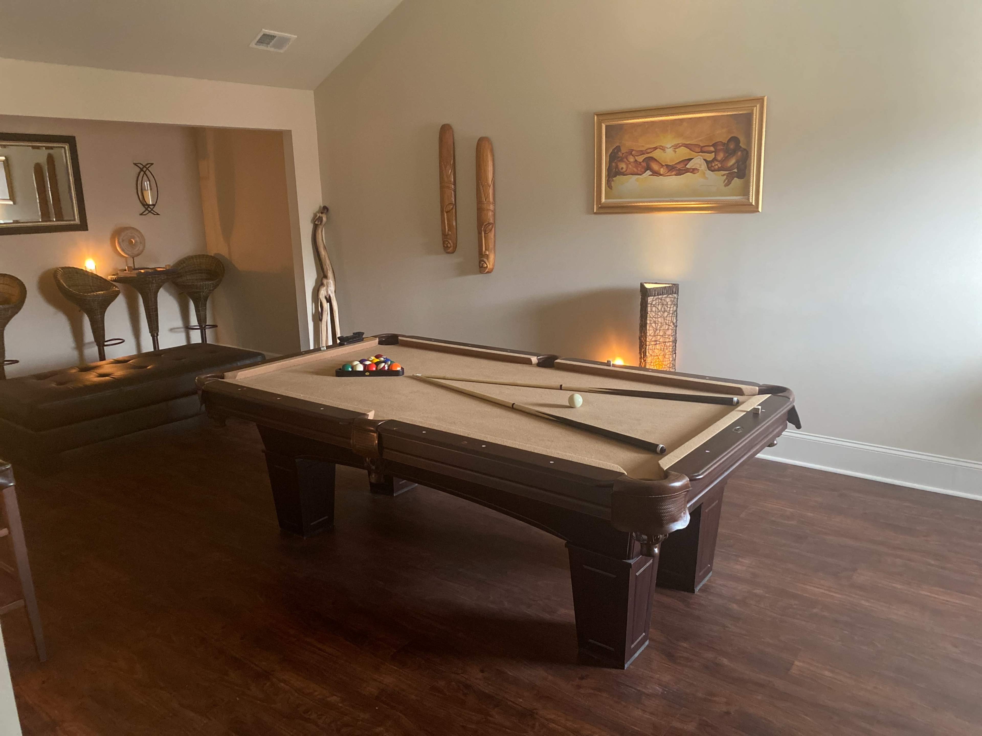 A room with a pool table in the center, surrounded by seating and decorative elements on the walls.