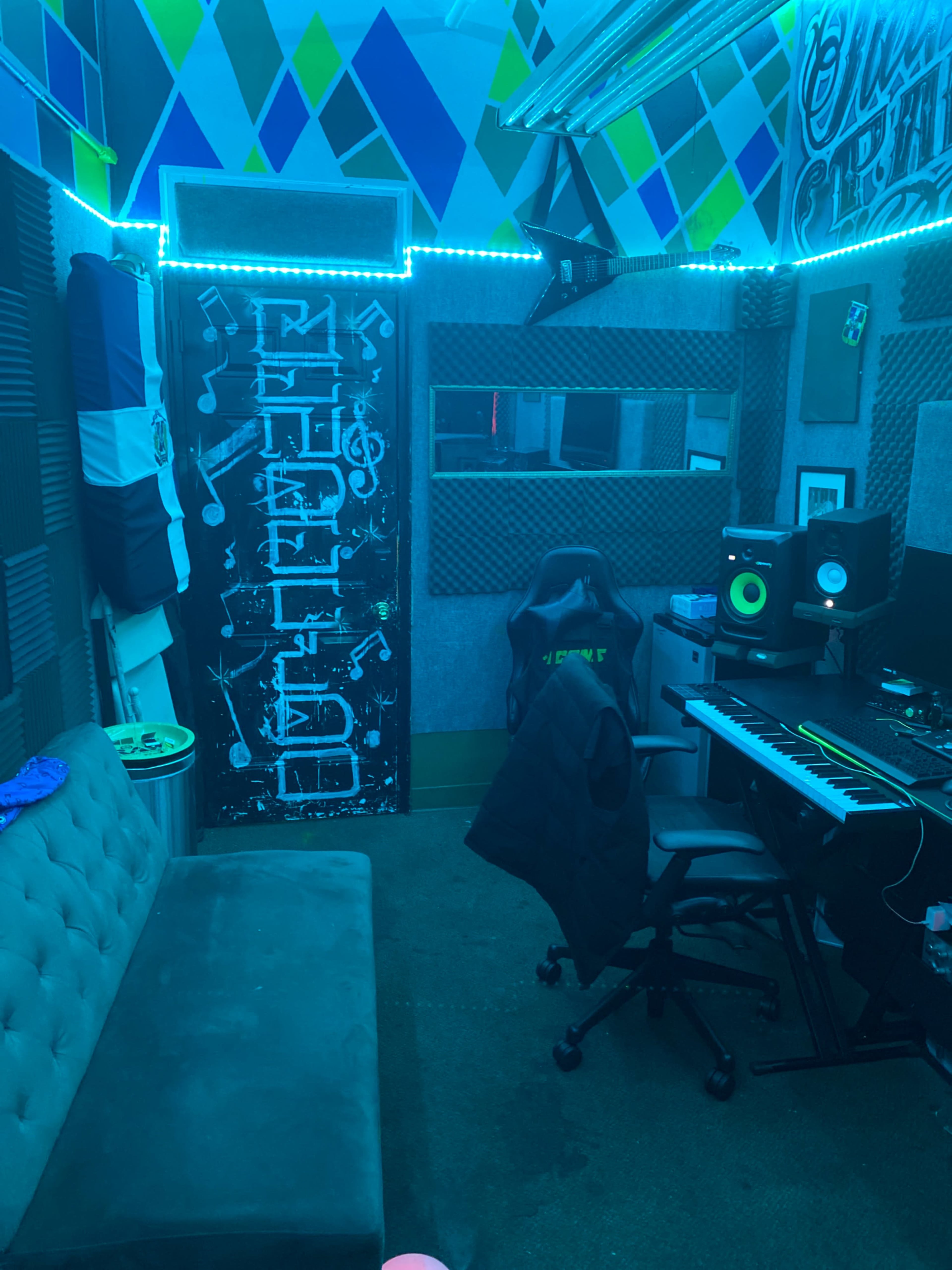 A music recording studio with a couch, a soundboard, a computer, and illuminated wall decorations.