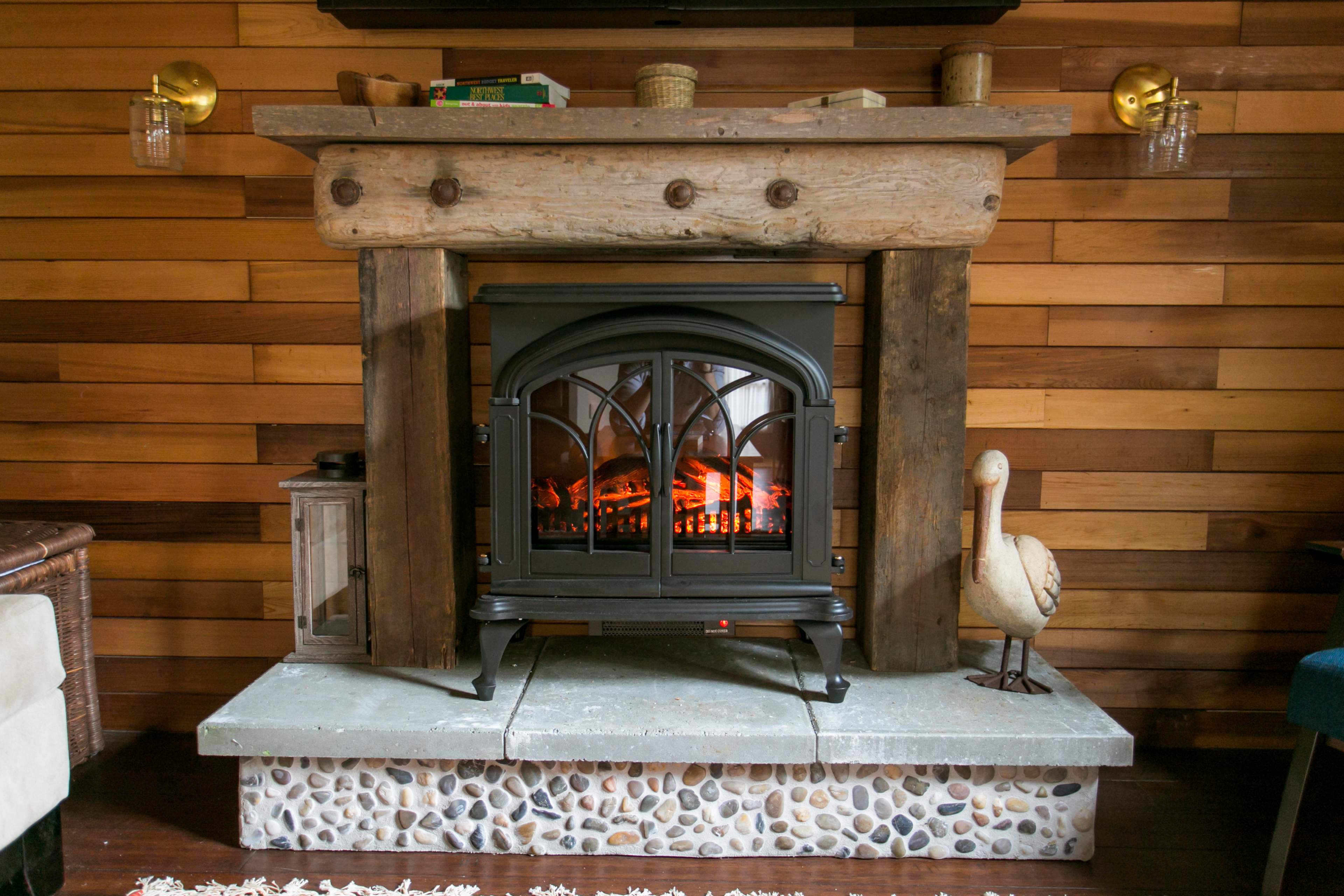 A black electric fireplace set within a rustic wooden mantel, surrounded by a stone base, with a decorative wooden duck nearby.