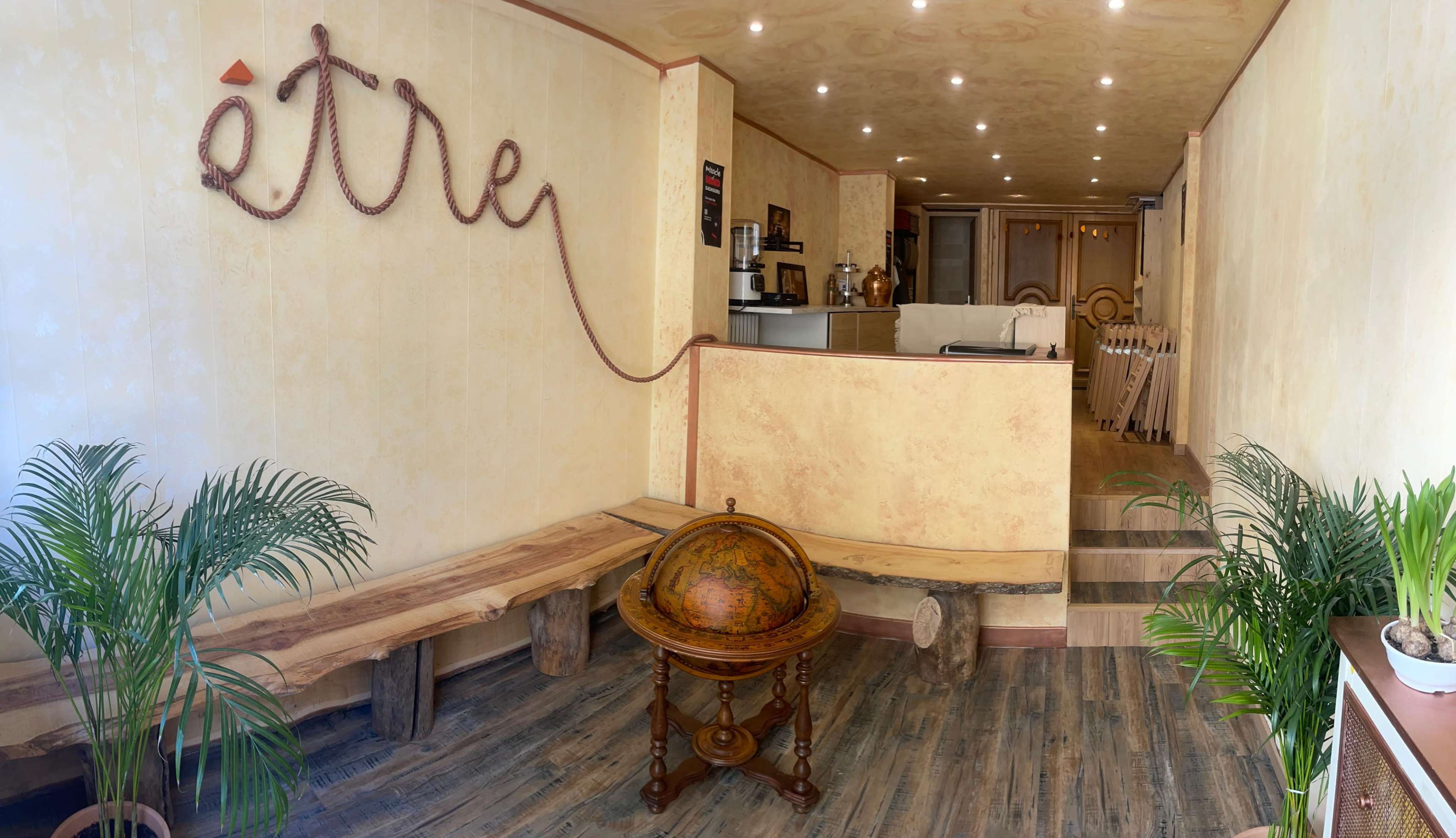 The image shows a cozy reception area with a wooden bench, a globe on a stand, and soft lighting illuminating the walls decorated with the word "être."