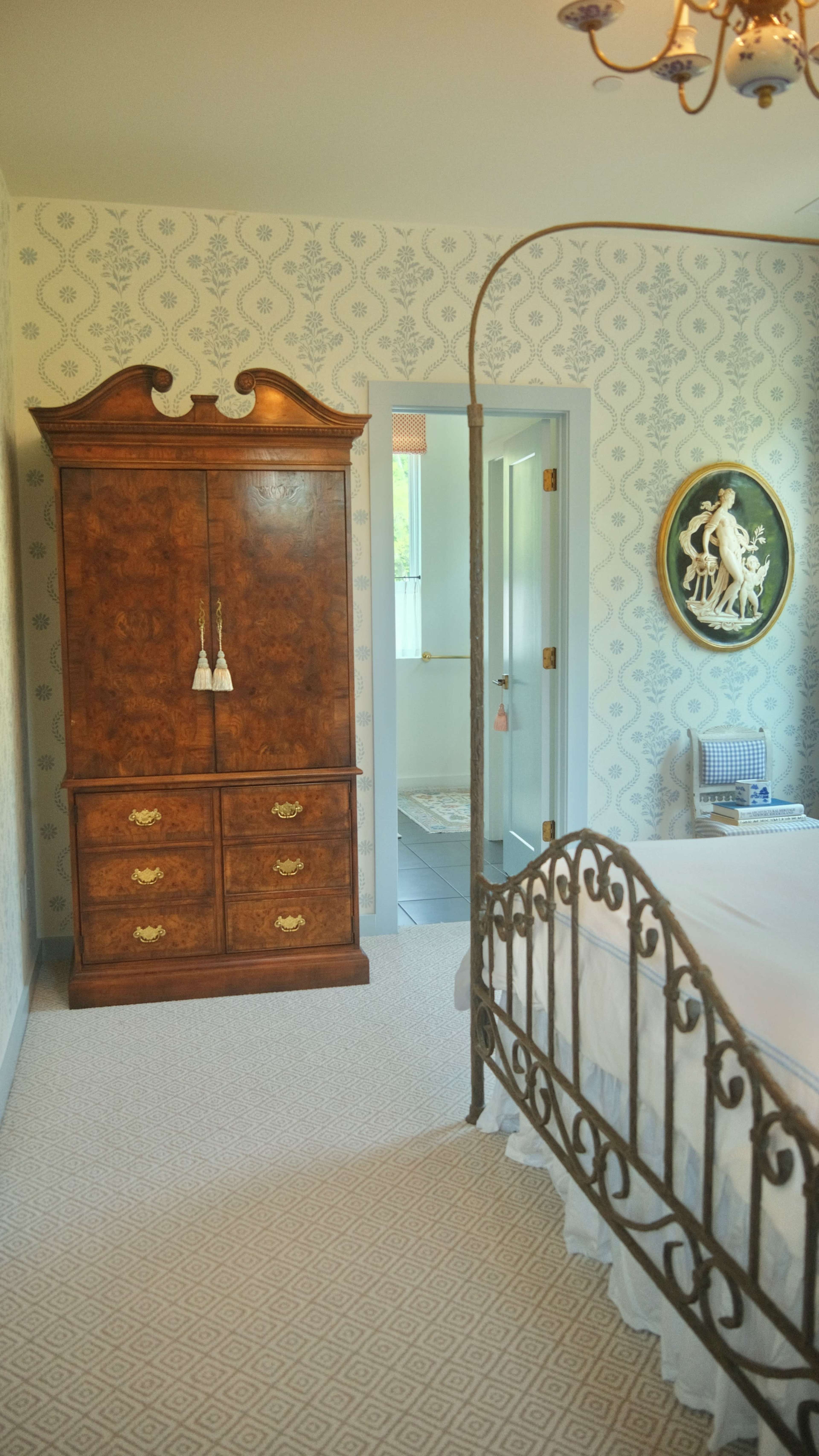 The image shows a bedroom featuring a vintage wooden wardrobe, an ornate metal bed frame, and patterned wallpaper.