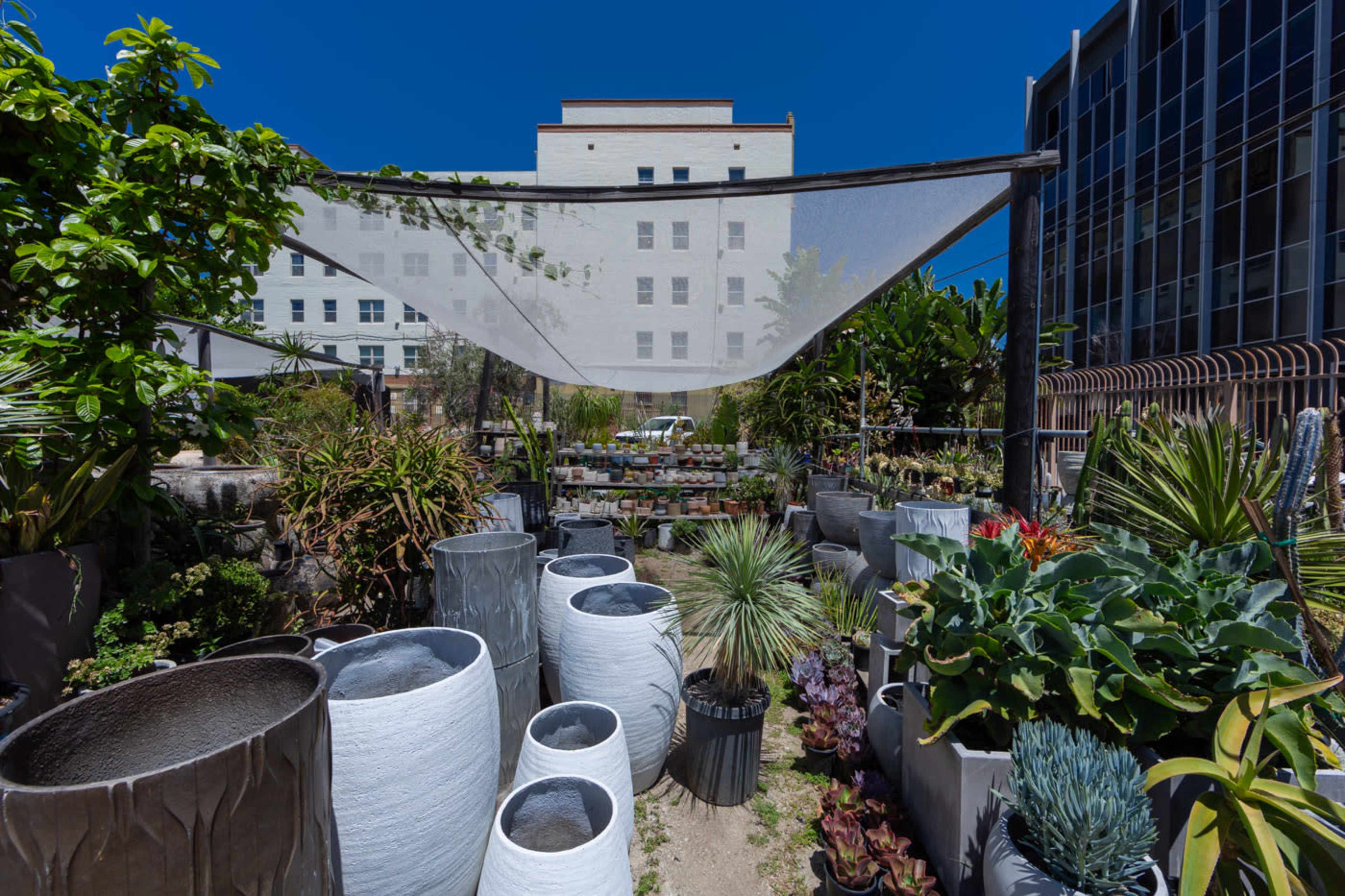 A garden filled with various plants and large decorative pots is partially shaded by a sheer canopy.