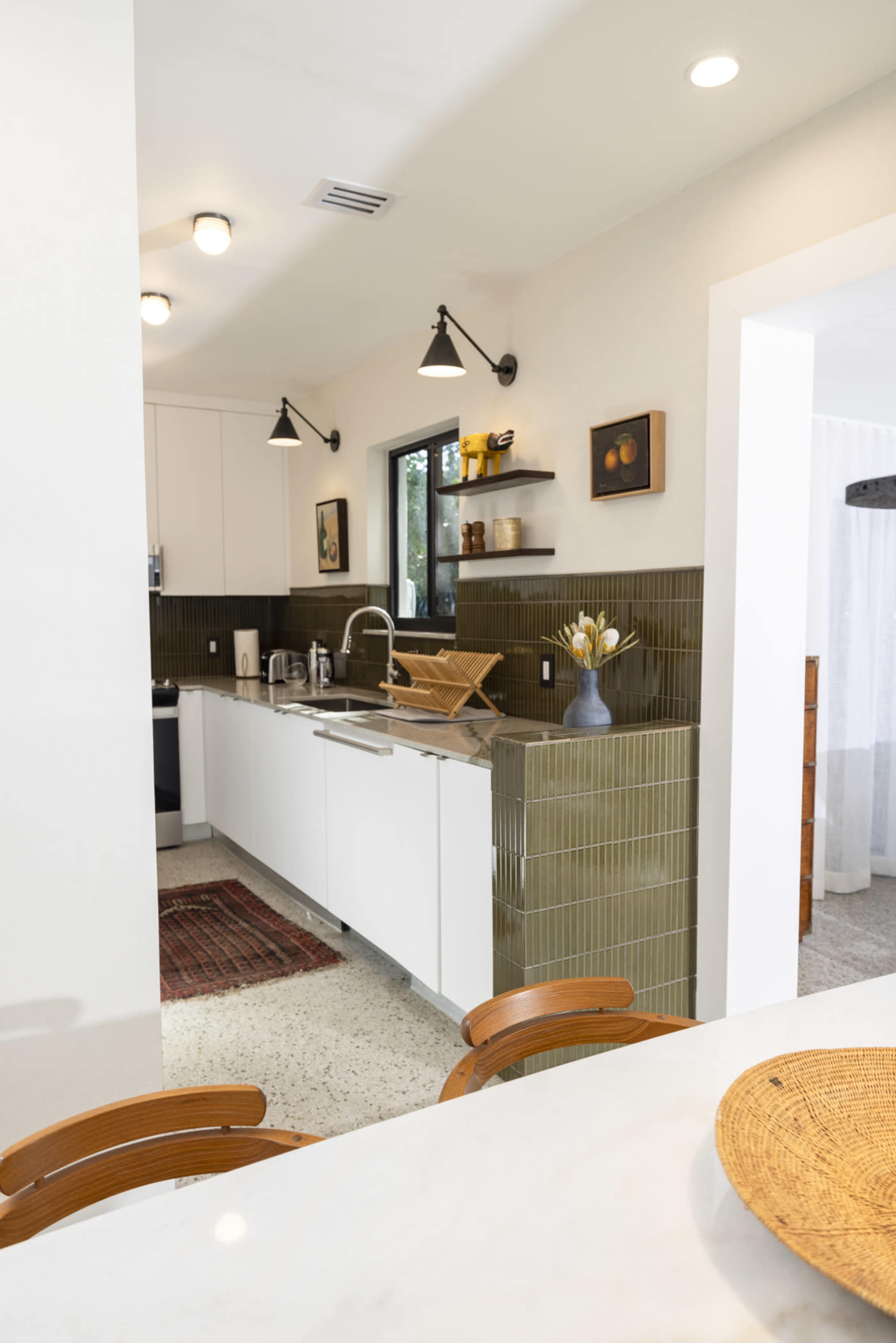 A modern kitchen with white cabinets, green tiled walls, and wooden shelves displaying decor.