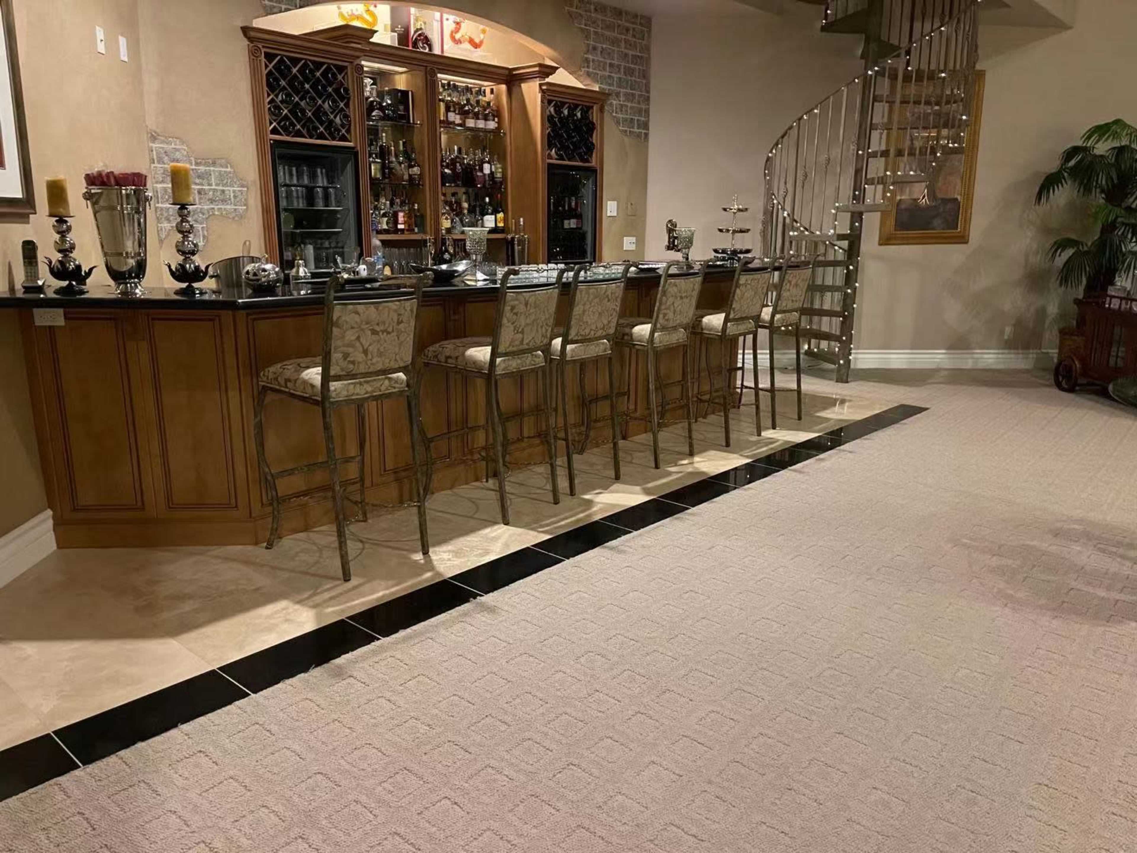 A home bar area with a countertop, several bar stools, and a spiral staircase in the background.