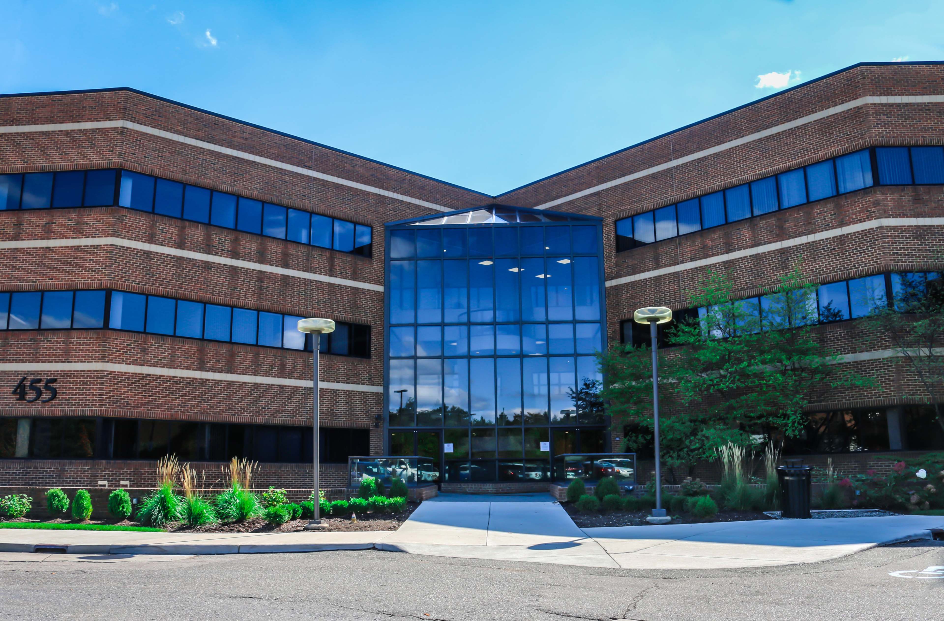 A three-story brick office building features a large glass entrance and a landscaped walkway.